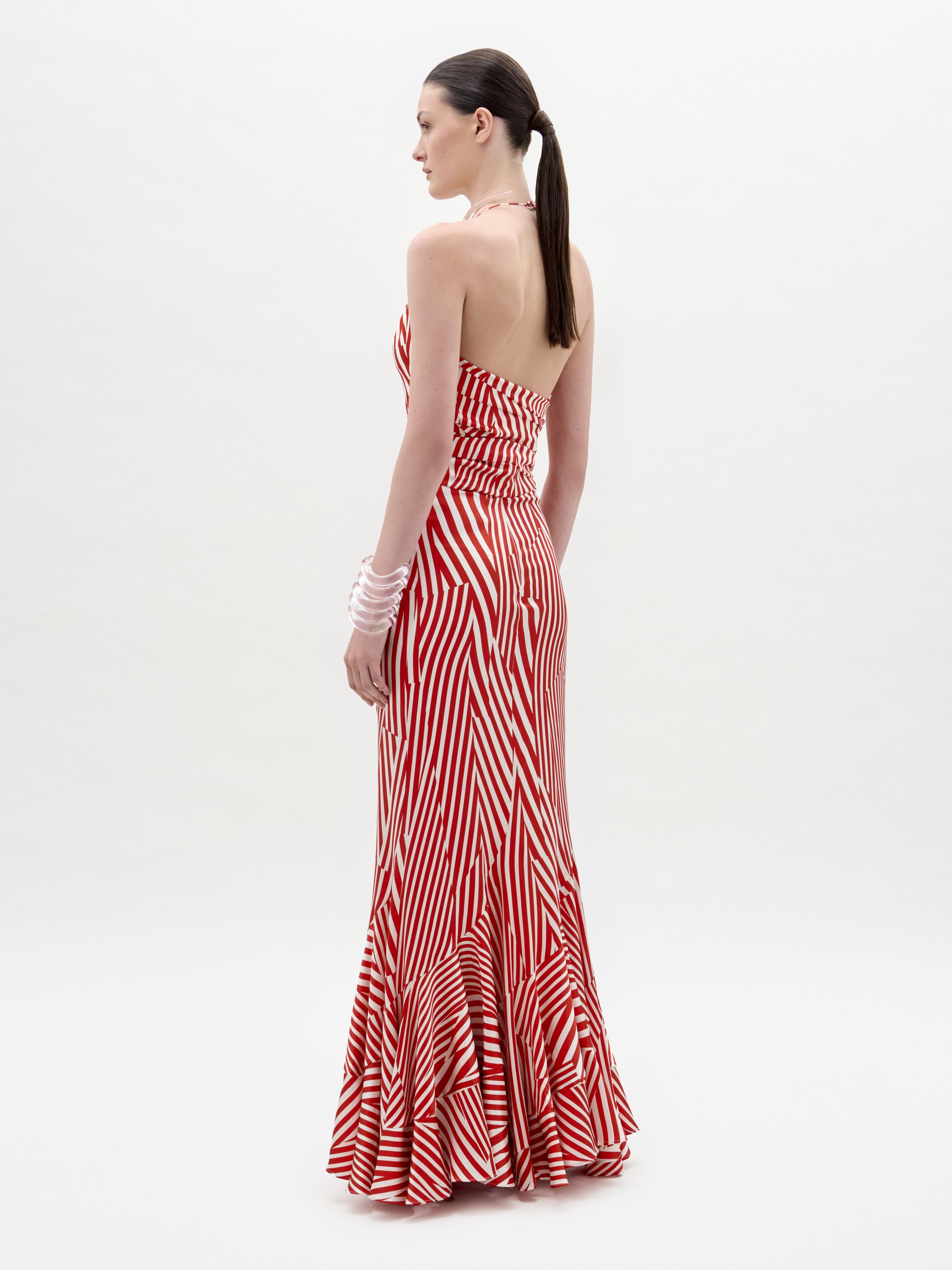 A woman with a ponytail wears the Florina Skirt—red and white striped, floor-length with a mermaid silhouette. She stands sideways, facing left, against a plain white background.
