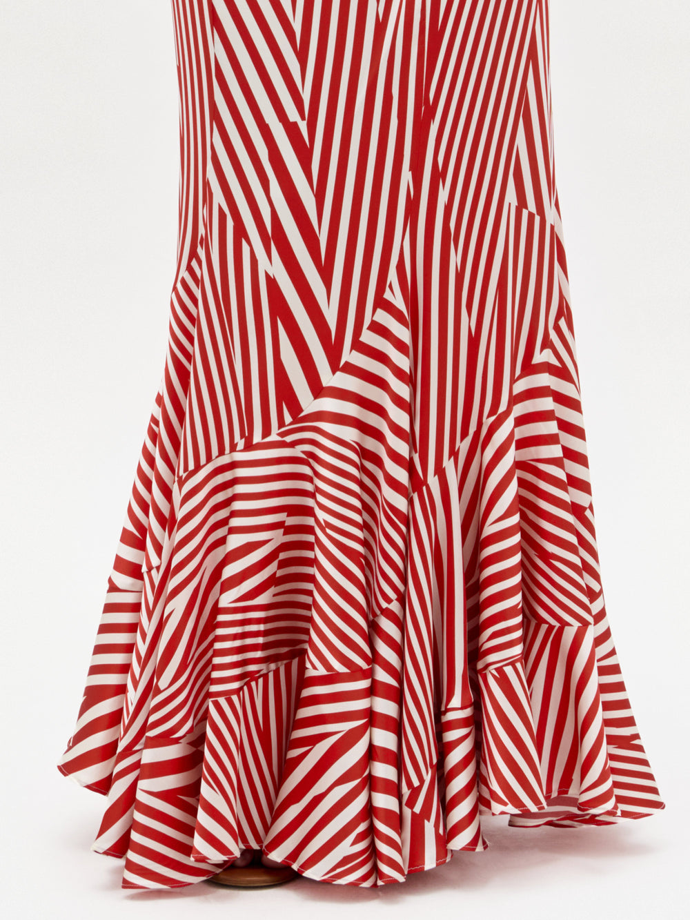 A woman stands against a plain white background wearing the Florina Skirt, a floor-length, red and white striped piece with a fitted waist and mermaid silhouette, crafted from luxurious Italian fabric.