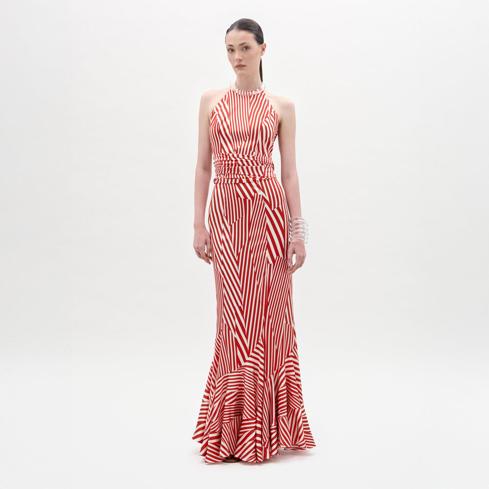 A woman stands against a plain white background wearing the Florina Skirt, a floor-length, red and white striped piece with a fitted waist and mermaid silhouette, crafted from luxurious Italian fabric.