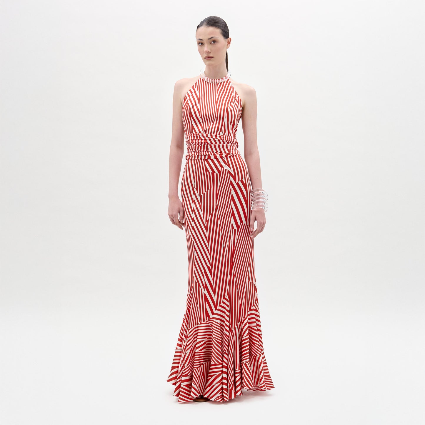 A woman stands against a plain white background wearing the Florina Skirt, a floor-length, red and white striped piece with a fitted waist and mermaid silhouette, crafted from luxurious Italian fabric.