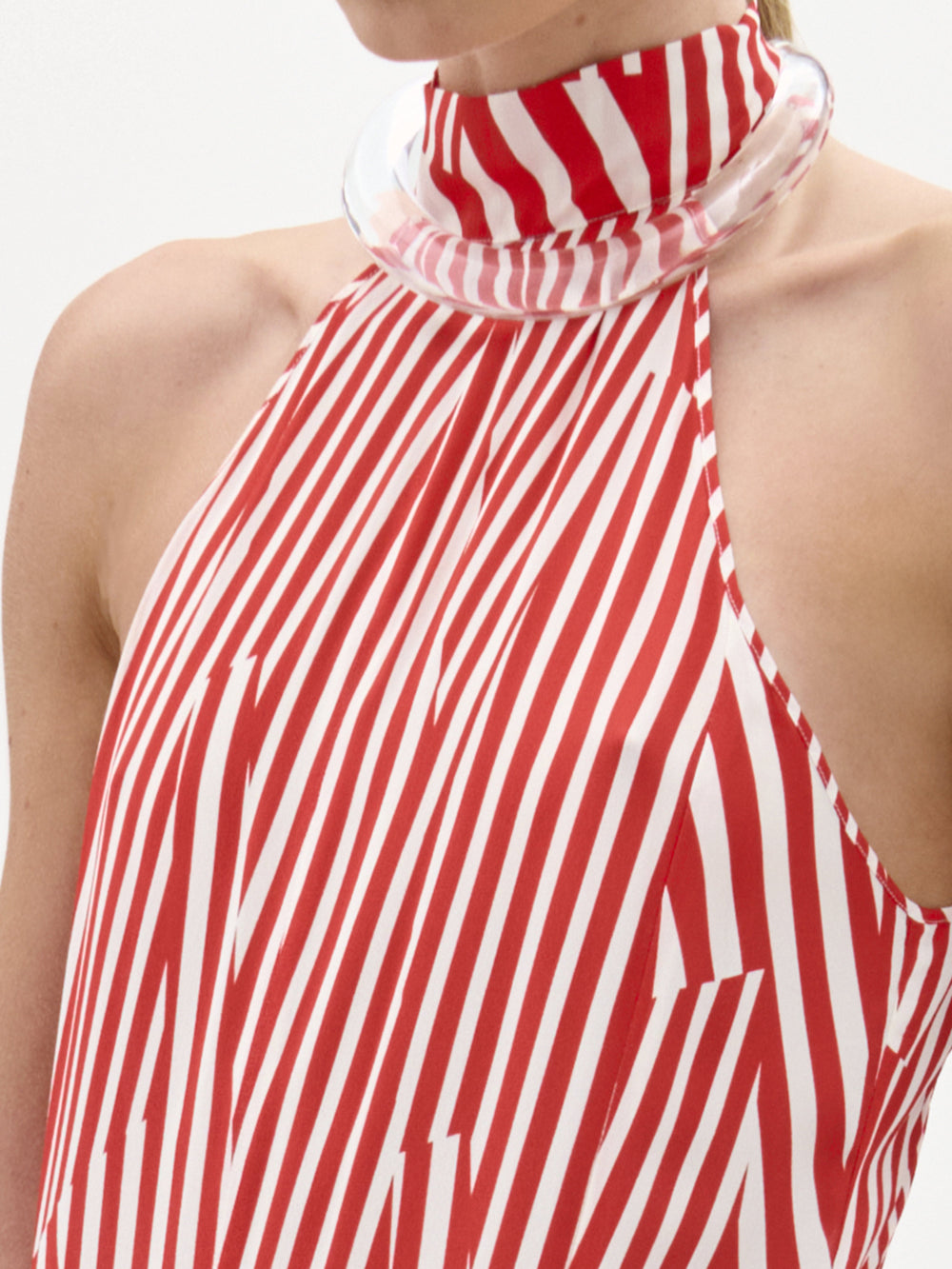 A woman wears the Koa Dress, a red and white striped halter neck maxi with an A-line silhouette, standing against a plain white background while holding a white towel and wearing sandals.