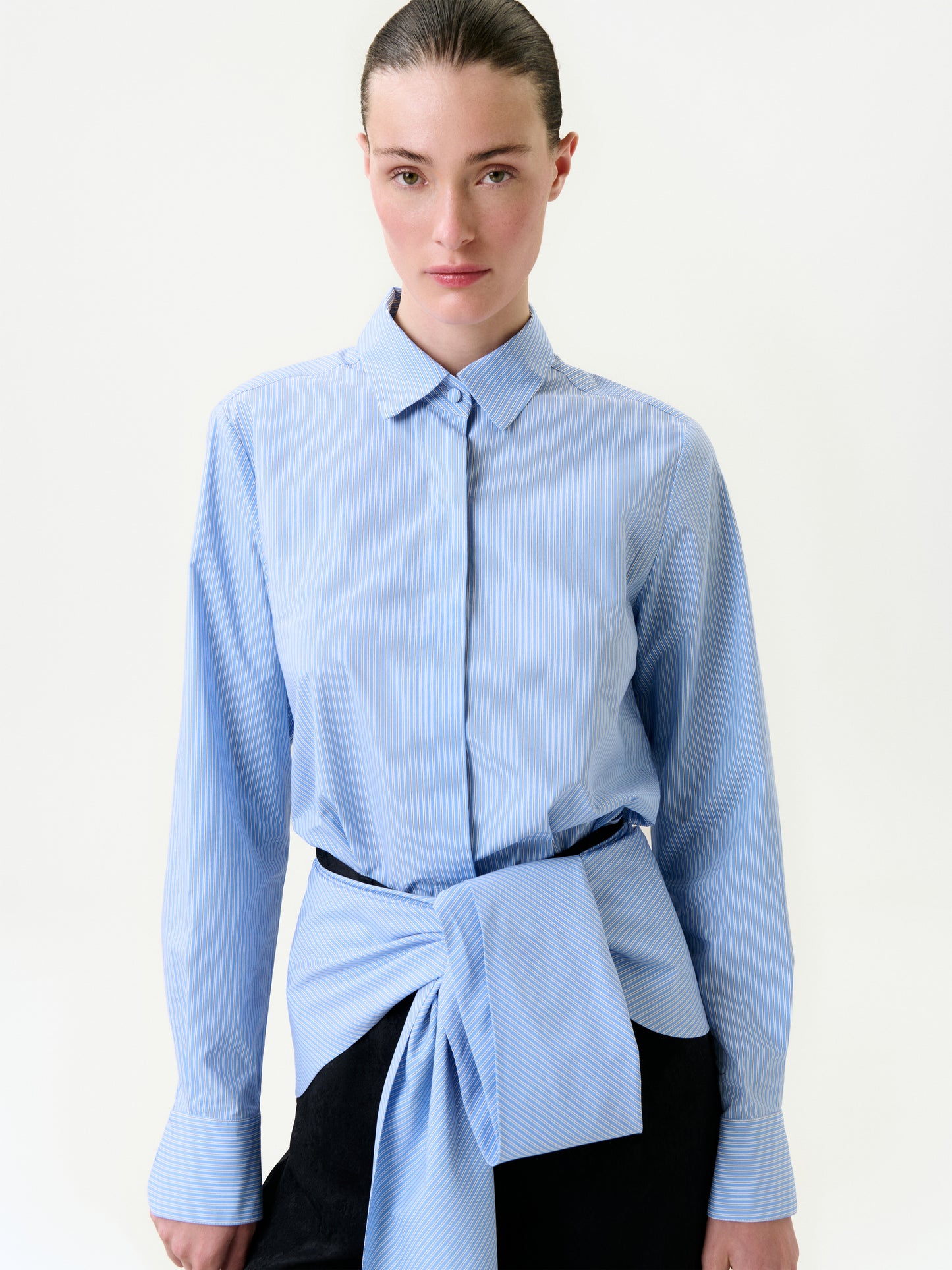 Woman wearing a blue striped shirt with a knot at the front on a white background