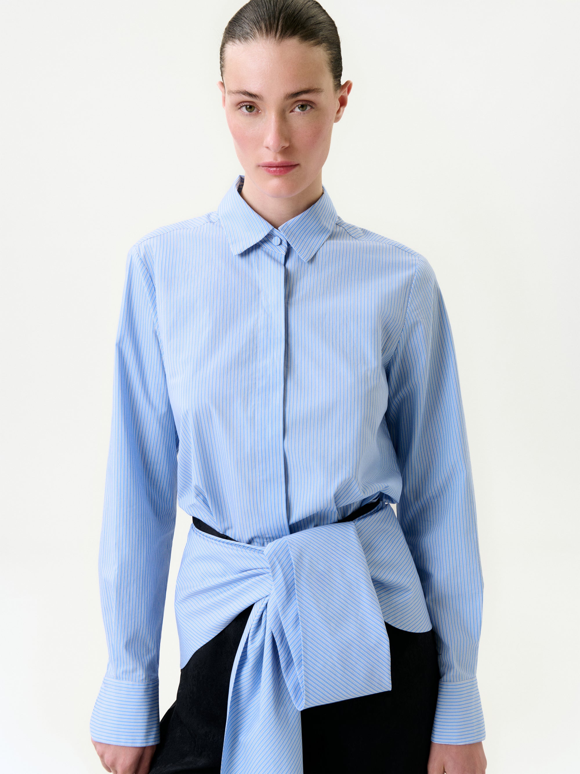 Woman wearing a blue striped shirt with a knot at the front on a white background