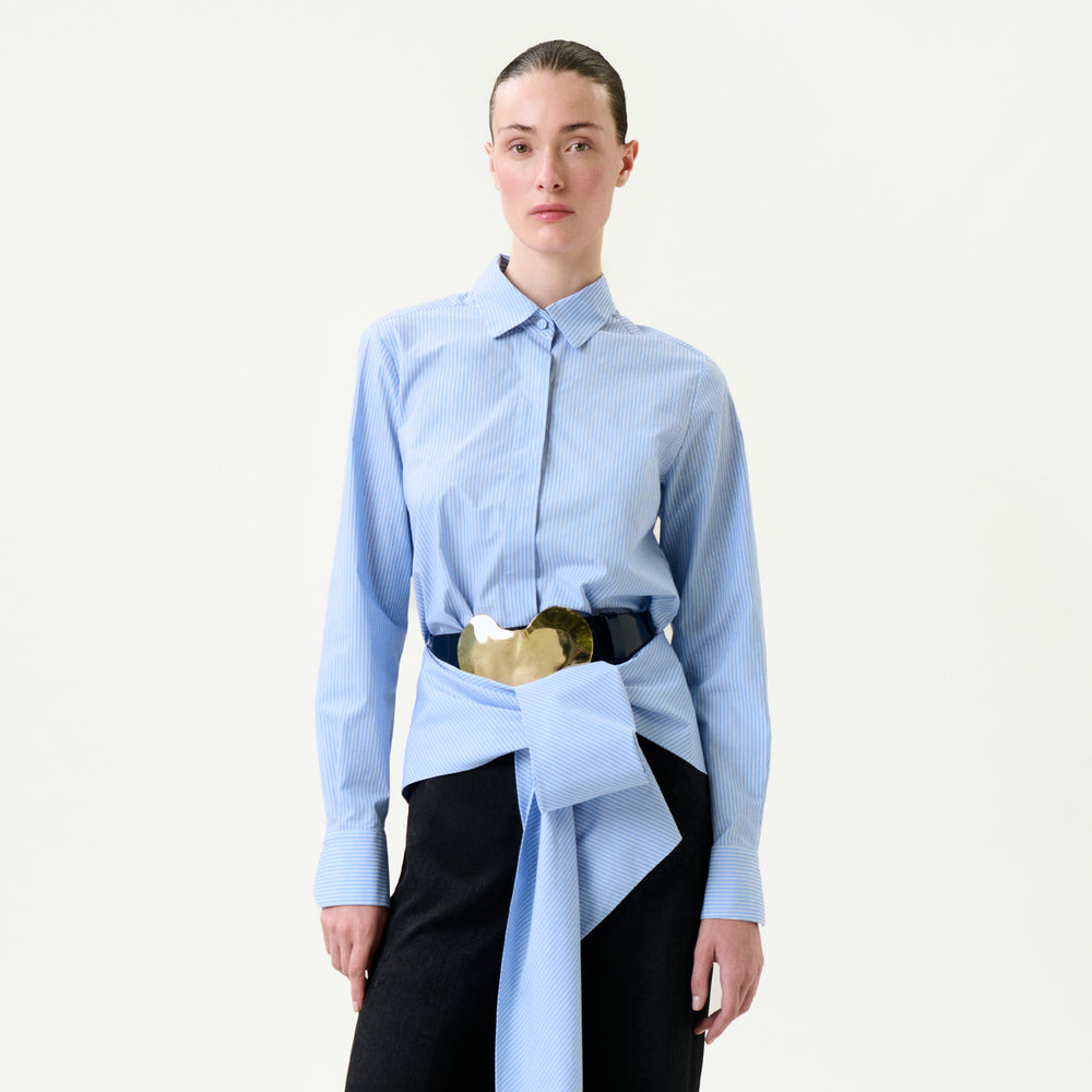 Person wearing a light blue shirt with a gold belt and black pants on a white background