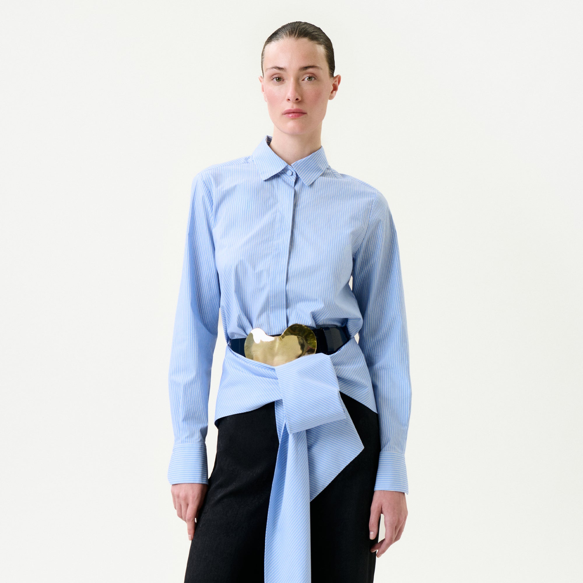 Person wearing a light blue shirt with a gold belt and black pants on a white background