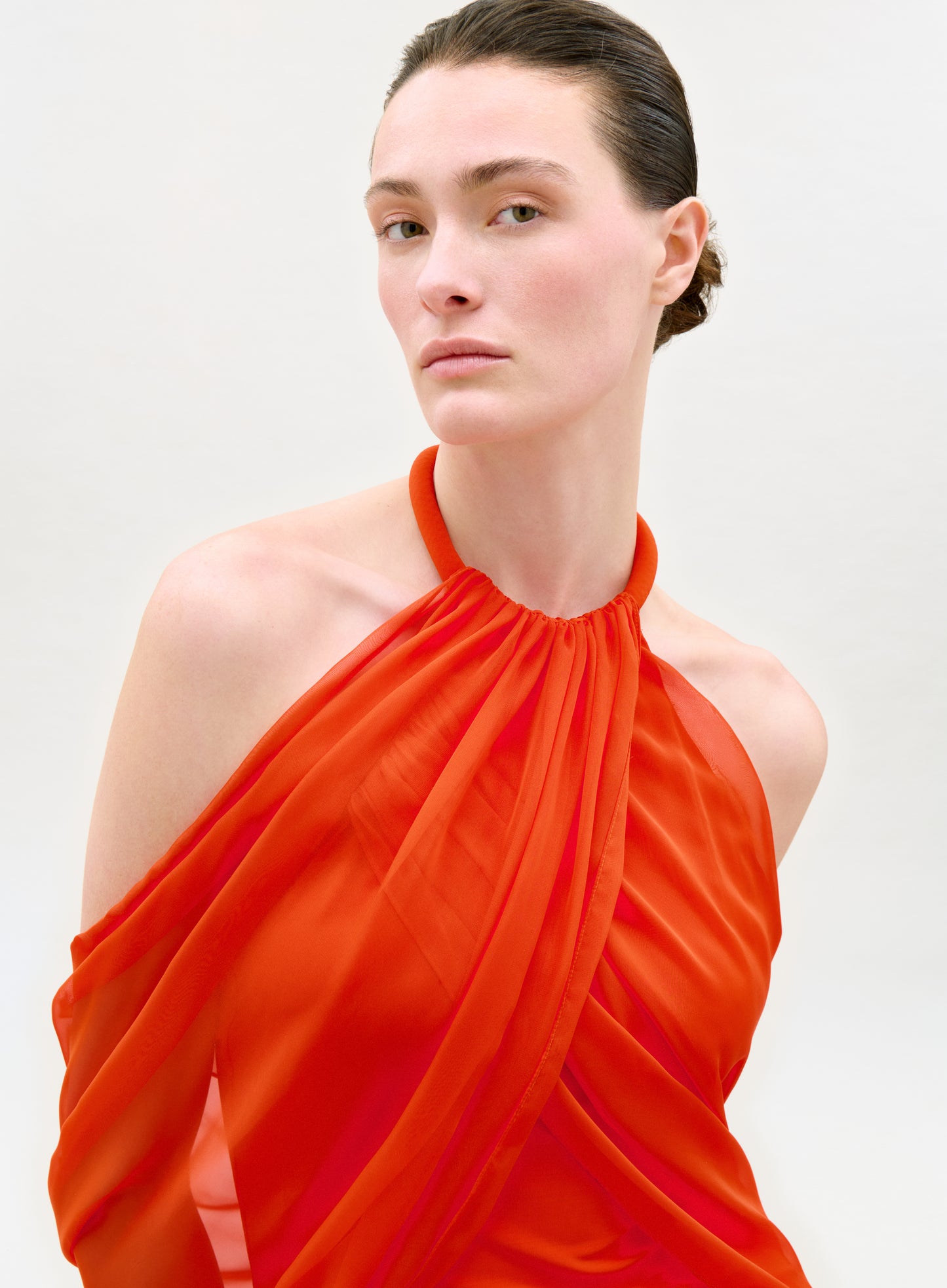 Woman wearing an orange halter neck dress against a white background