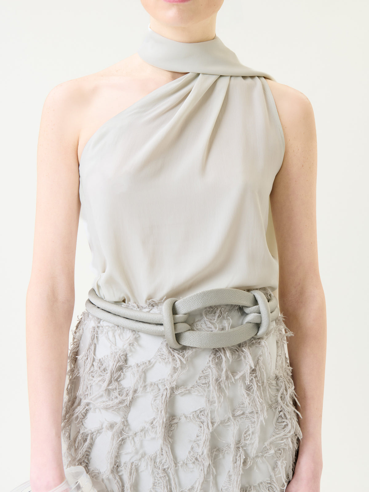 Wearing the Onora Blouse in light gray, accented by a matching wide belt and paired with a textured, fringed skirt, the person embodies a soft and elegant look. Their face is partially out of frame.
