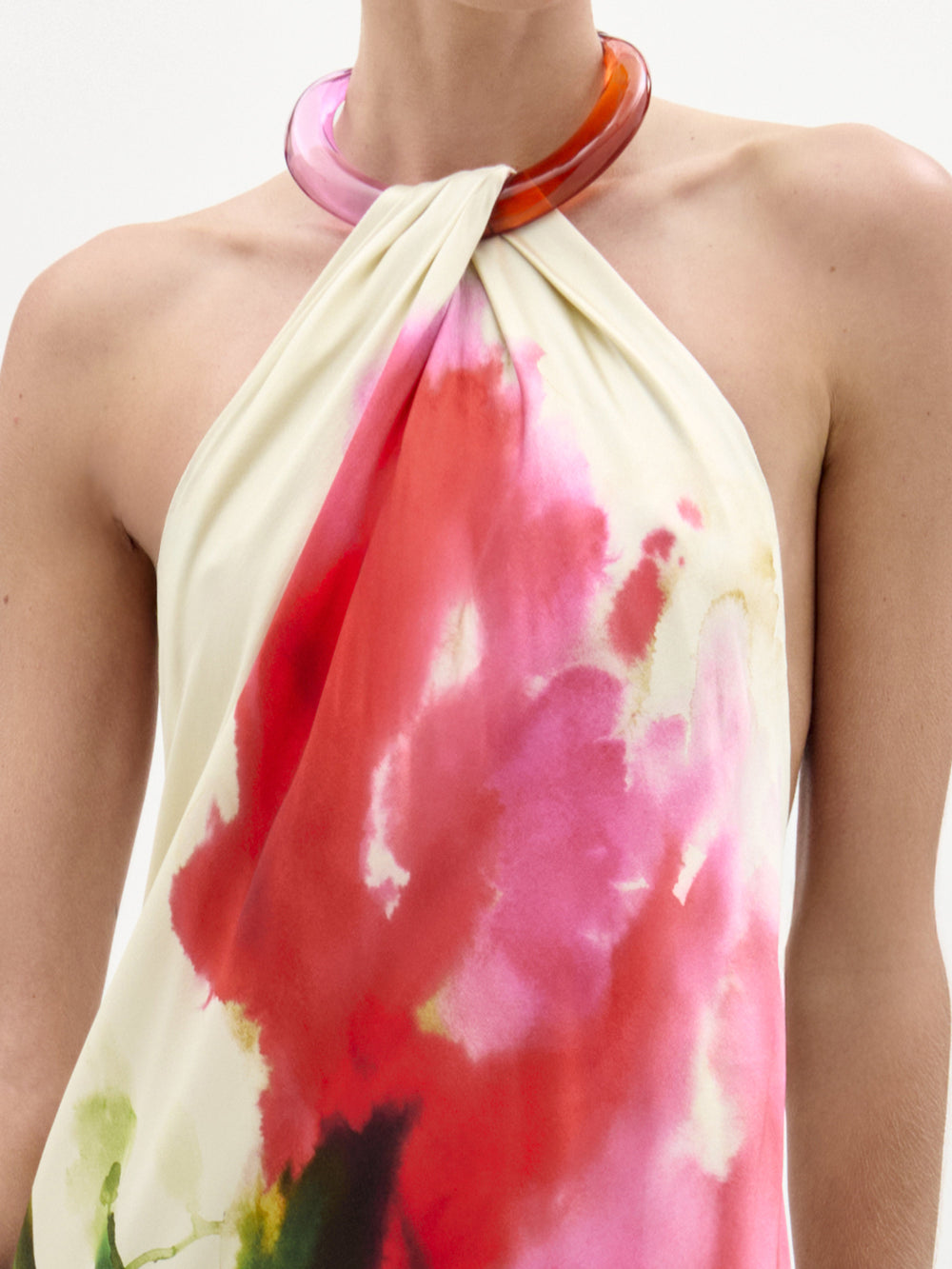 A woman stands against a plain background wearing the Jesse Dress, a sleeveless cream maxi with a colorful abstract floral print and halter neckline, paired with open-toe heels.