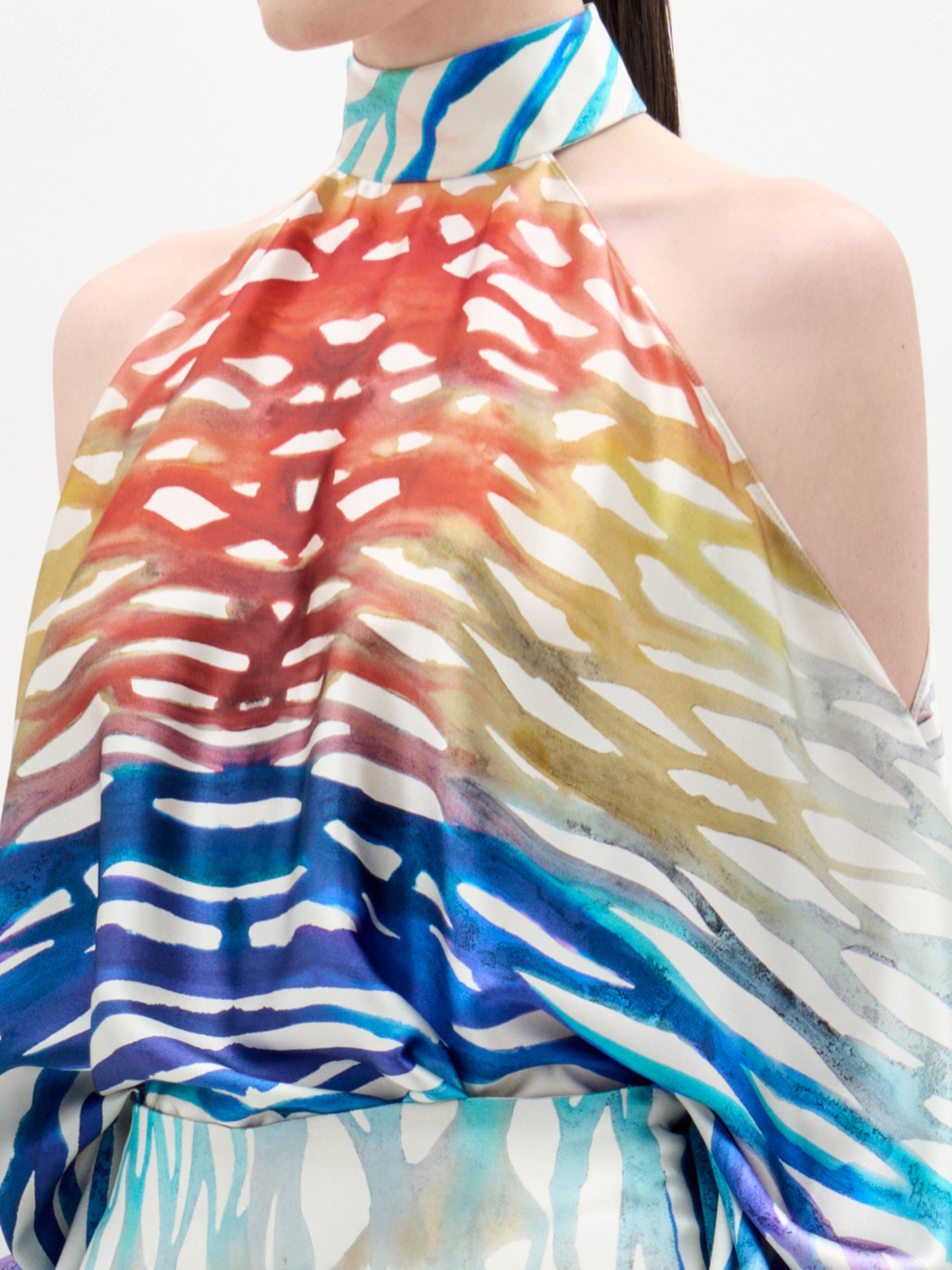 A woman models the Safira Blouse—an off-shoulder top featuring a colorful, abstract print in luxe Italian fabric—paired with matching wide-leg pants, set against a plain white background.