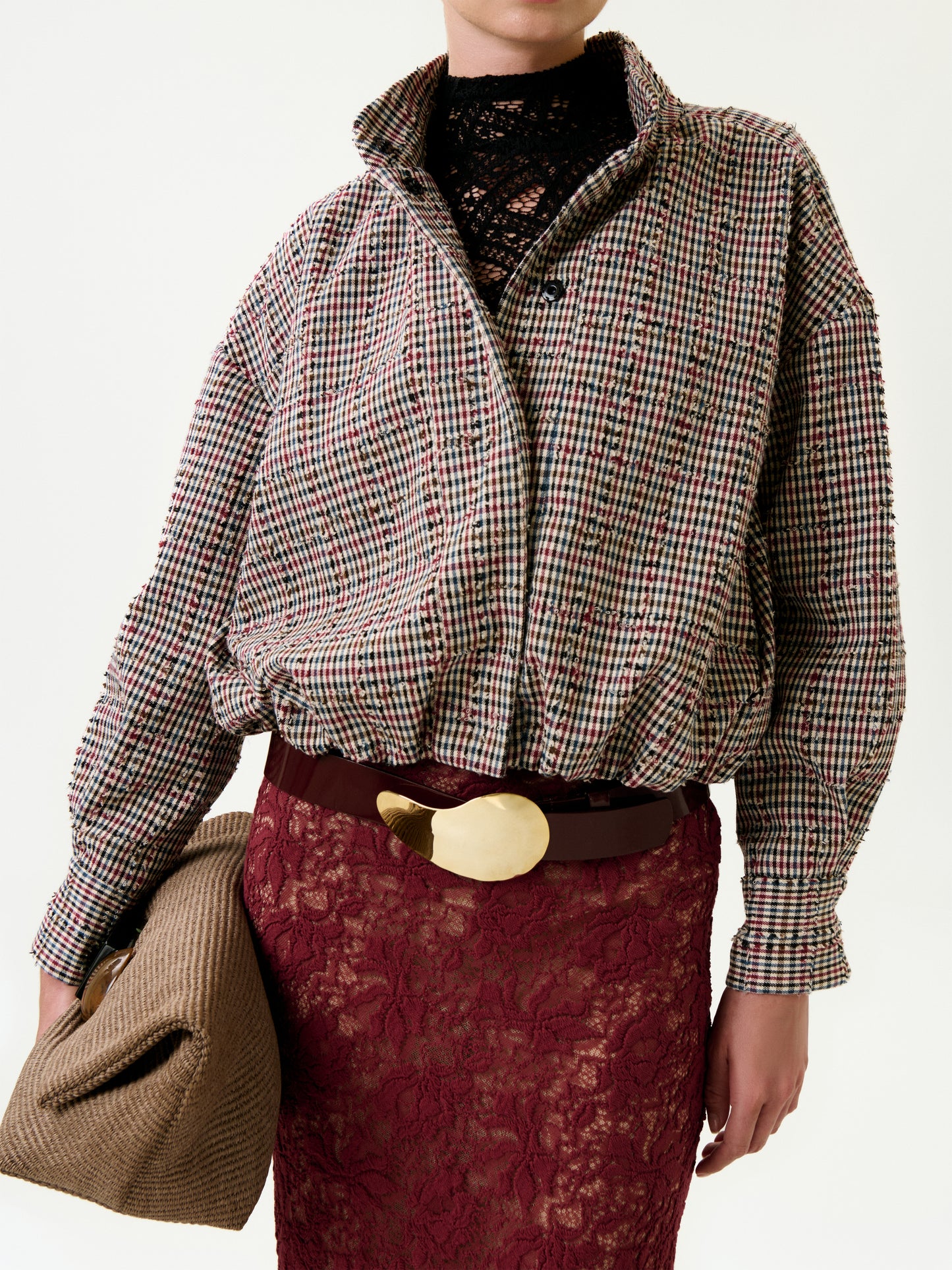 Person wears the Julinka Jacket styled in an oversized fit over a loose plaid shirt, black lace top, burgundy lace skirt, brown belt with gold buckle, and holds a brown textured bag against a plain white background.