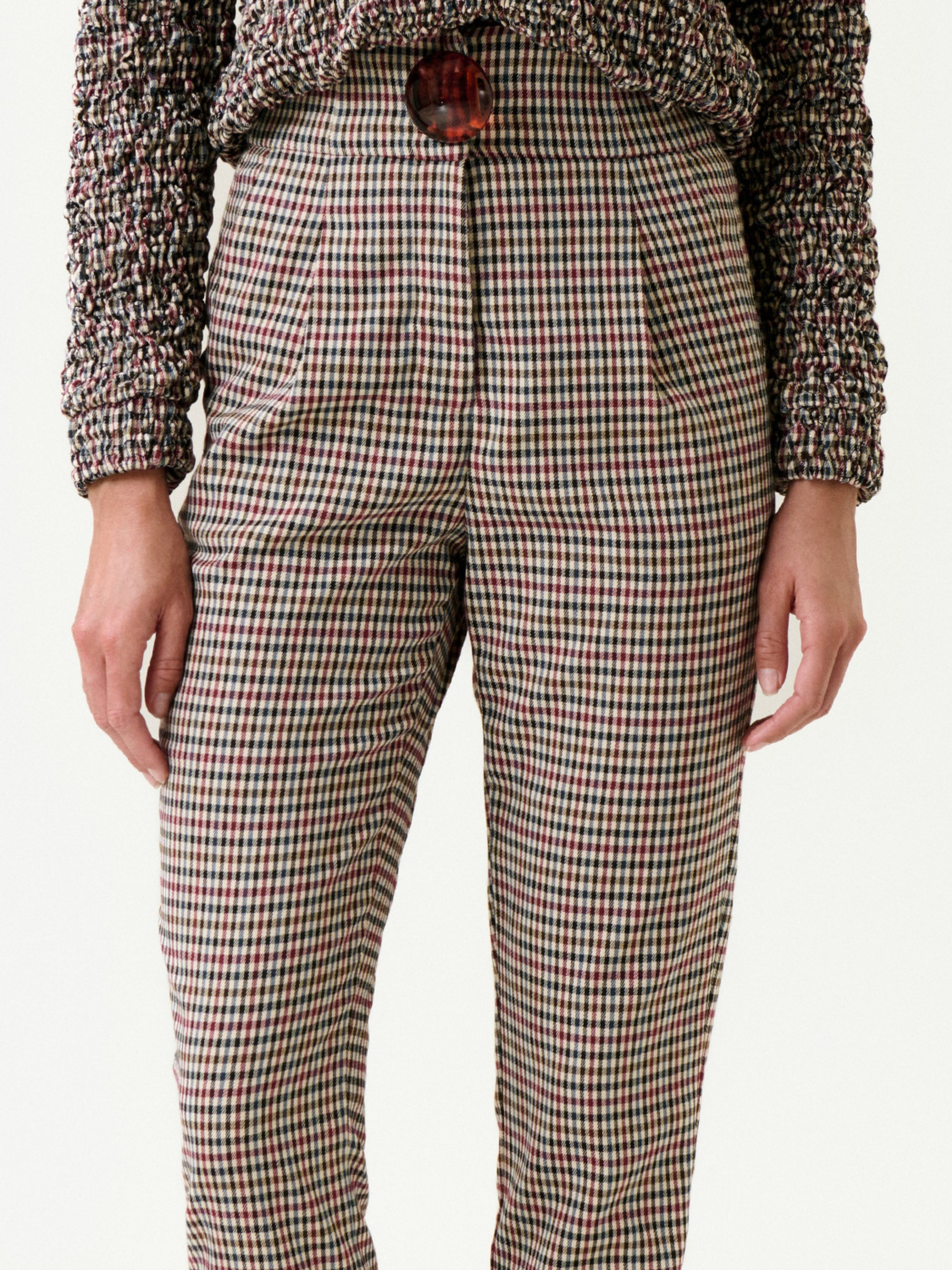A person is wearing the Luca Pant—high-waisted, plaid with pleats and a large button, made from Italian fabric for a true-to-size fit—paired with a textured, multicolored sweater. The image shows the torso to mid-thigh.