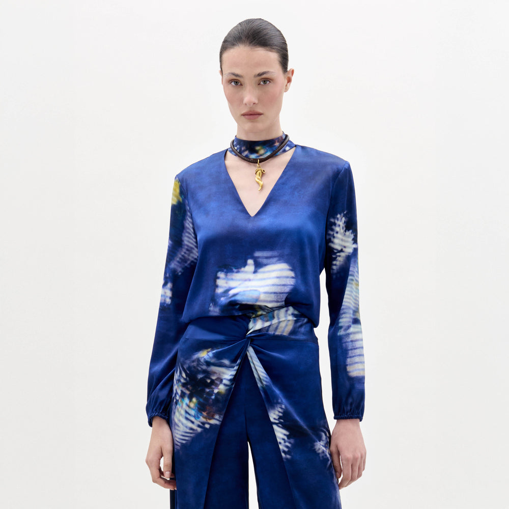 Woman wearing the Lane Blouse, a blue patterned top, paired with a matching skirt and choker necklace, standing against a plain light background.