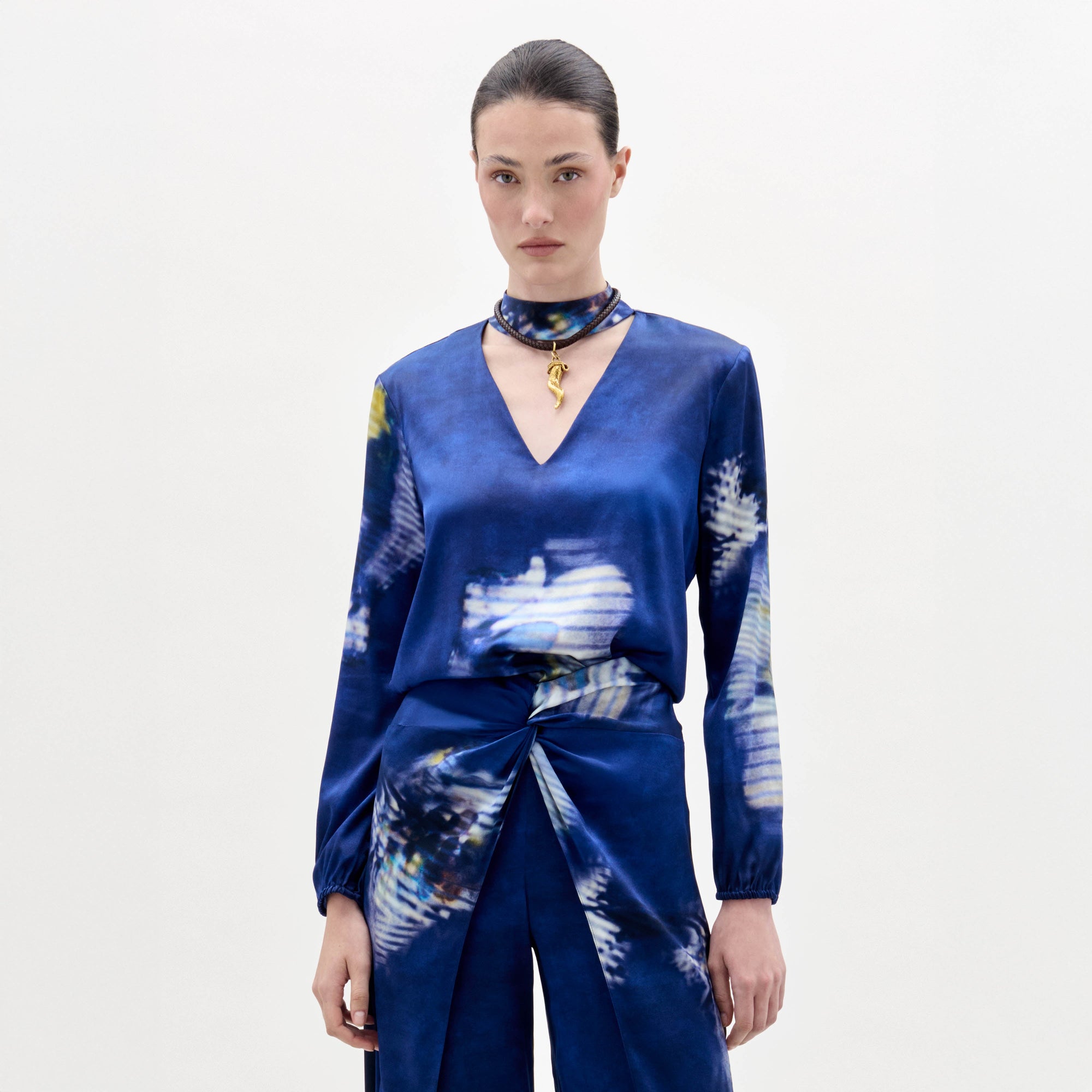 Woman wearing the Lane Blouse, a blue patterned top, paired with a matching skirt and choker necklace, standing against a plain light background.