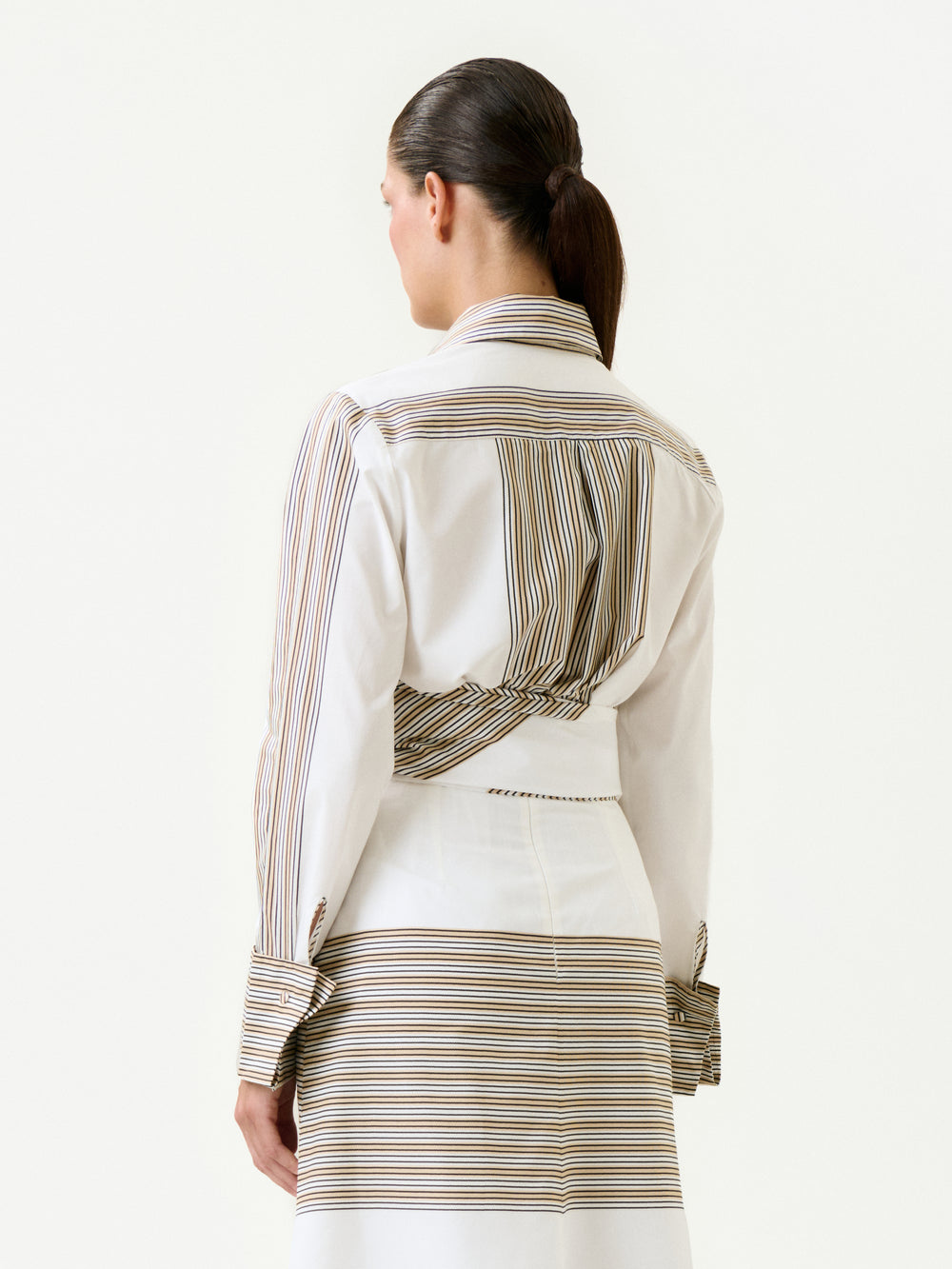 A woman with dark hair in a low ponytail is shown from the back, wearing the 100% cotton Angeles Shirt in soft Italian fabric with stripes and a matching skirt against a plain, light background.