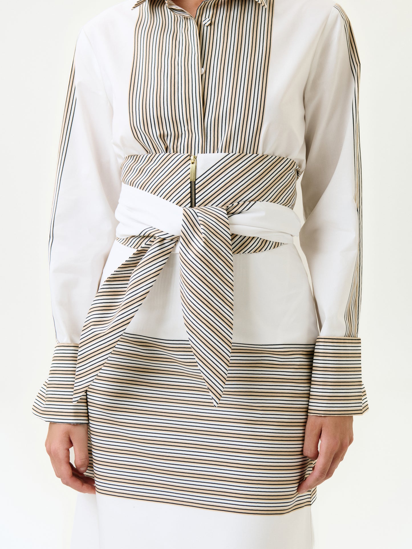 A person wears the Angeles Shirt, a 100% cotton white shirt with vertical brown and black stripes, paired with a matching striped skirt and a wide striped belt at the waist. Only the torso and arms are shown.
