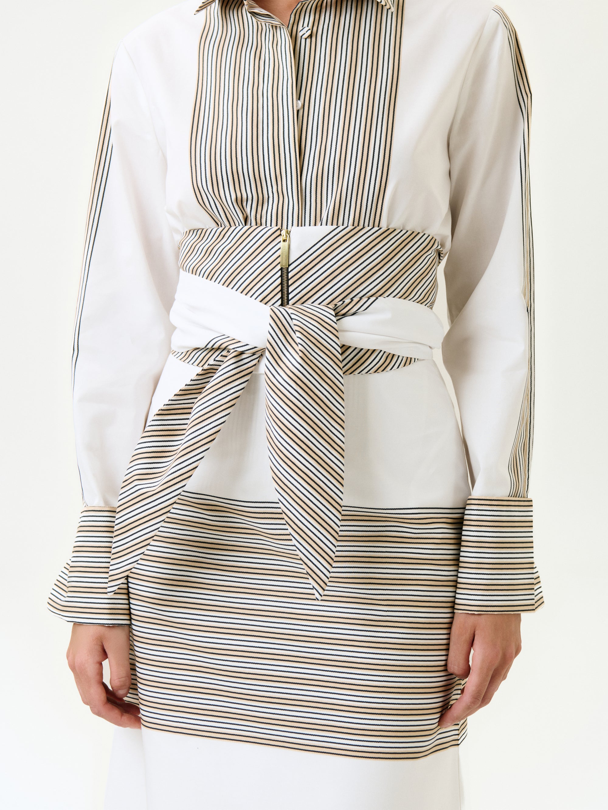 A person wearing the Lyla Skirt, featuring horizontal stripes and bold waistband details, paired with a white shirt with thin black and gold vertical stripes in 100% Italian cotton and a wide detachable belt tied at the waist.