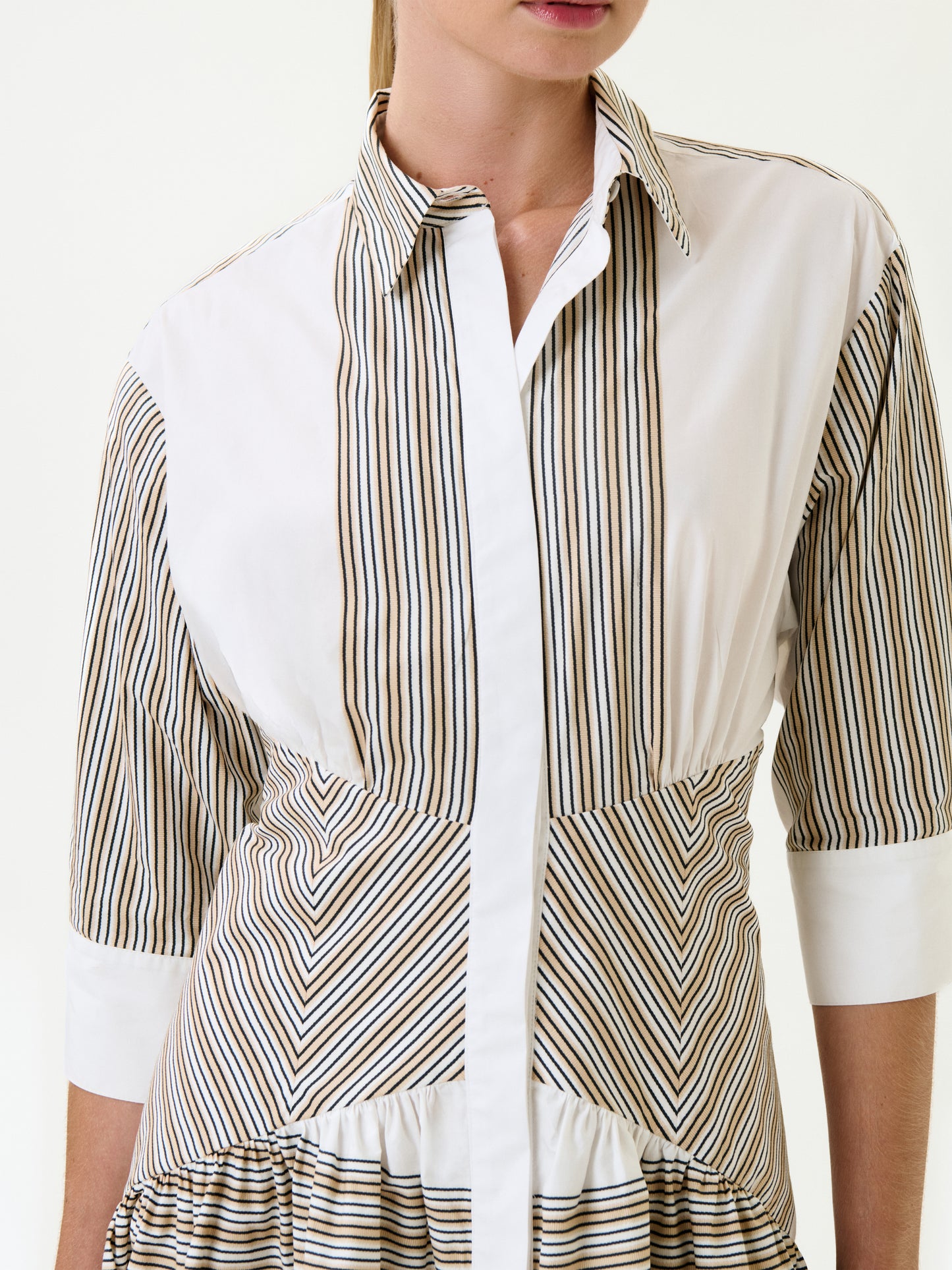 The woman wears the Indy Dress, a white button-up midi dress with vertical and diagonal brown and black stripes in 100% Italian cotton. Featuring a collared neckline and three-quarter sleeves, her face is partially out of frame.
