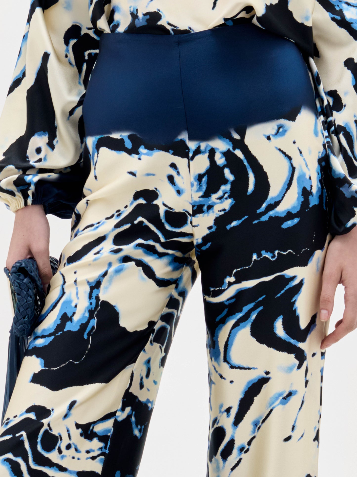 A woman stands against a plain white background wearing a cream and navy blue marble-patterned halter top with matching Como Pants in a wide-leg style.