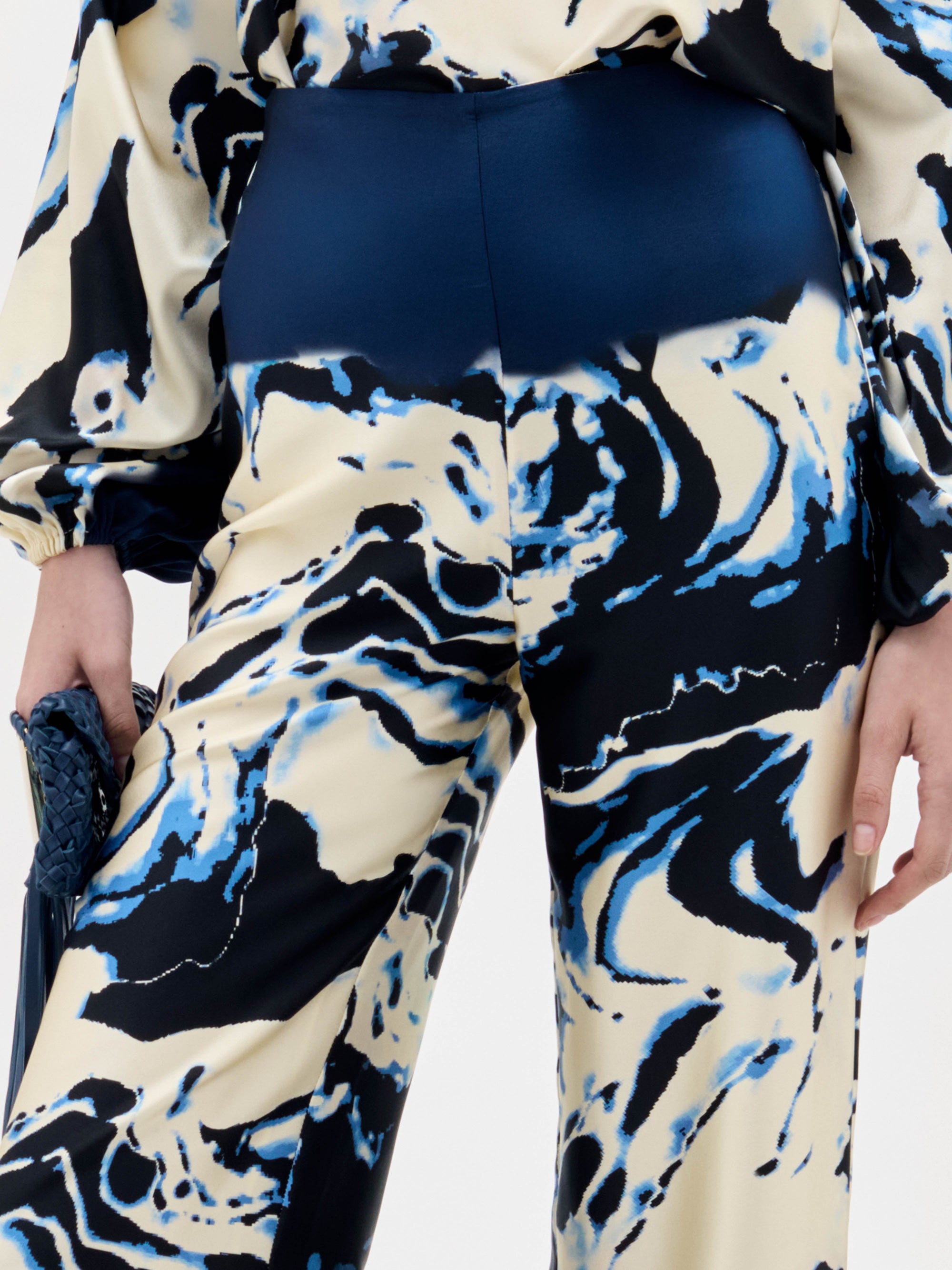 A woman stands against a plain white background wearing a cream and navy blue marble-patterned halter top with matching Como Pants in a wide-leg style.