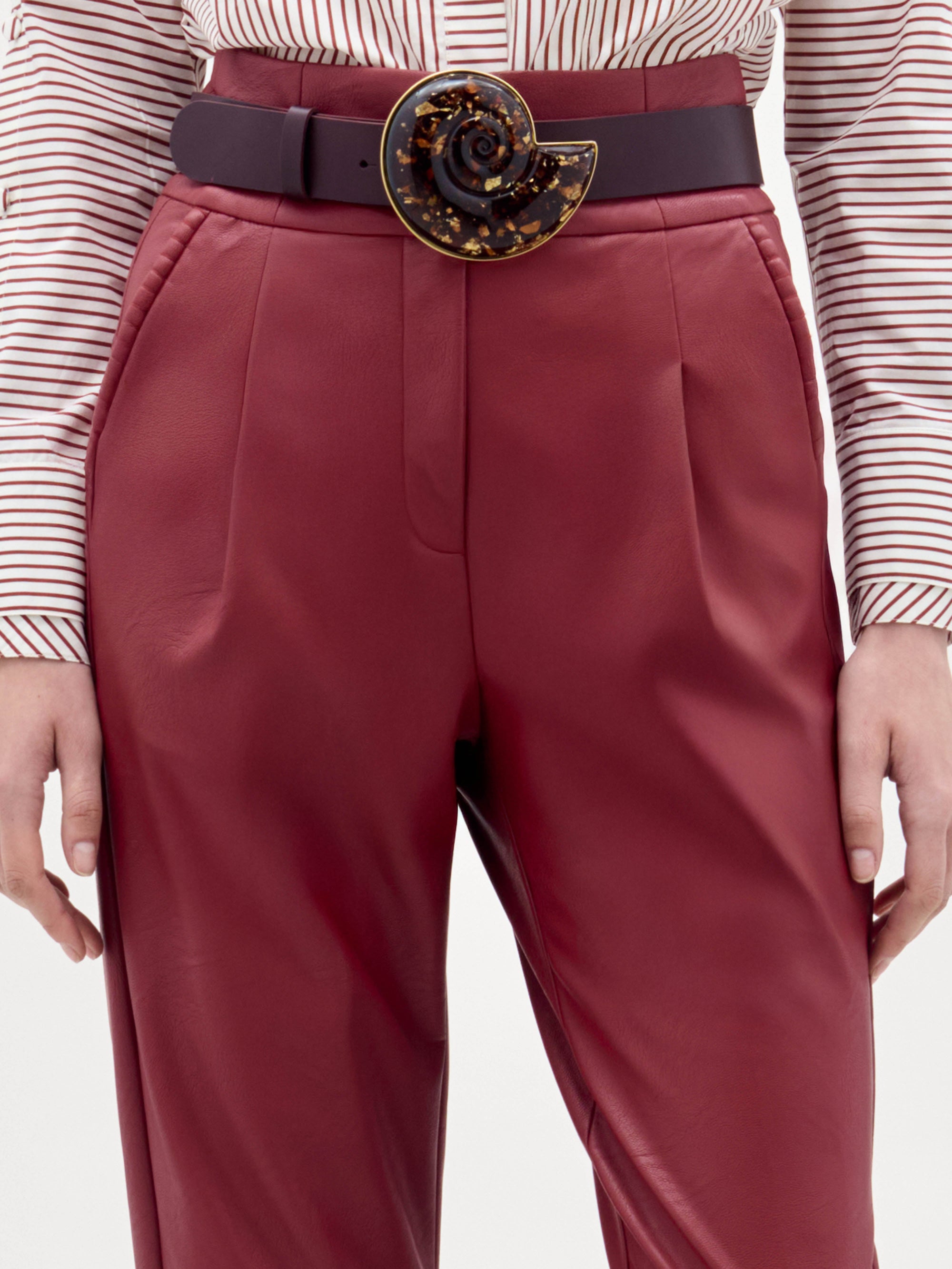 A woman stands against a plain background wearing high-waisted red Moad Pants, a striped shirt with a large red flower applique, a wide belt, and black heeled sandals.