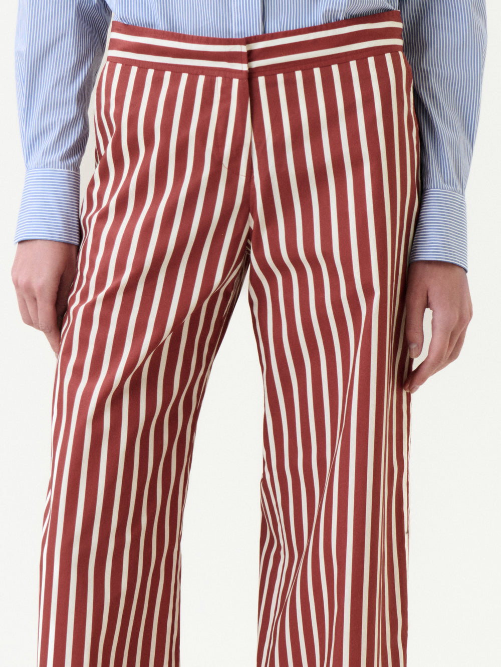 Wearing the Ulla Pant in red and white vertical stripes, paired with a blue and white pinstriped shirt. Made from 100% cotton, this look blends comfort and effortless style, shown from waist to mid-thigh.