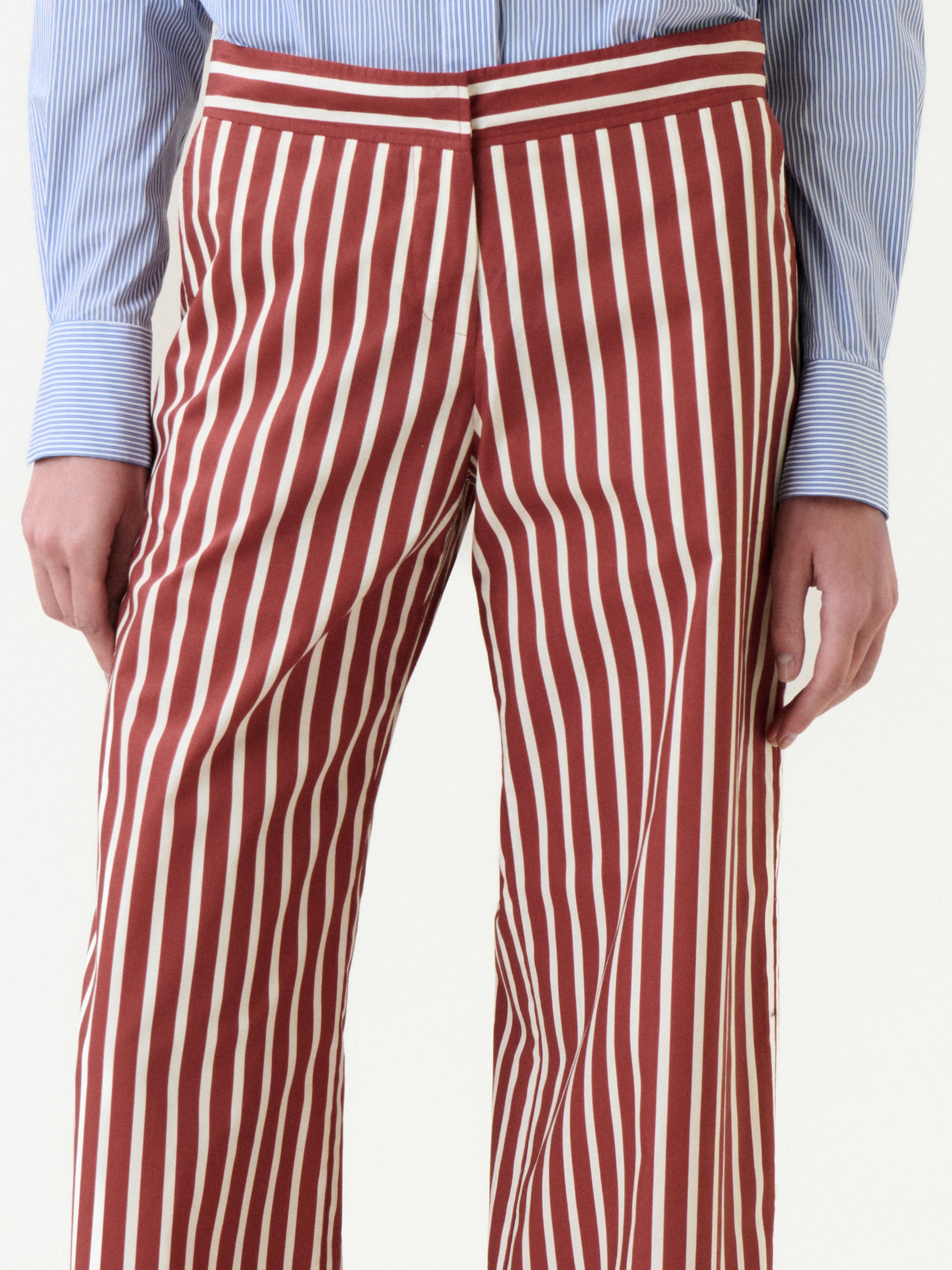 Wearing the Ulla Pant in red and white vertical stripes, paired with a blue and white pinstriped shirt. Made from 100% cotton, this look blends comfort and effortless style, shown from waist to mid-thigh.