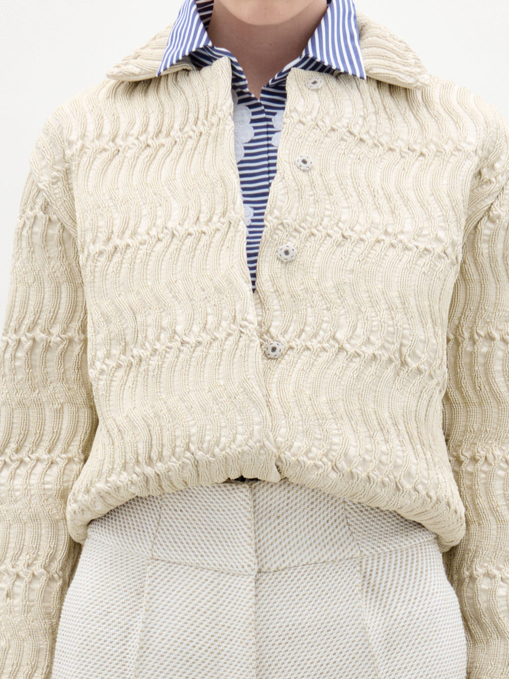 Close-up of a person wearing a cream knitted cardigan over a striped shirt.