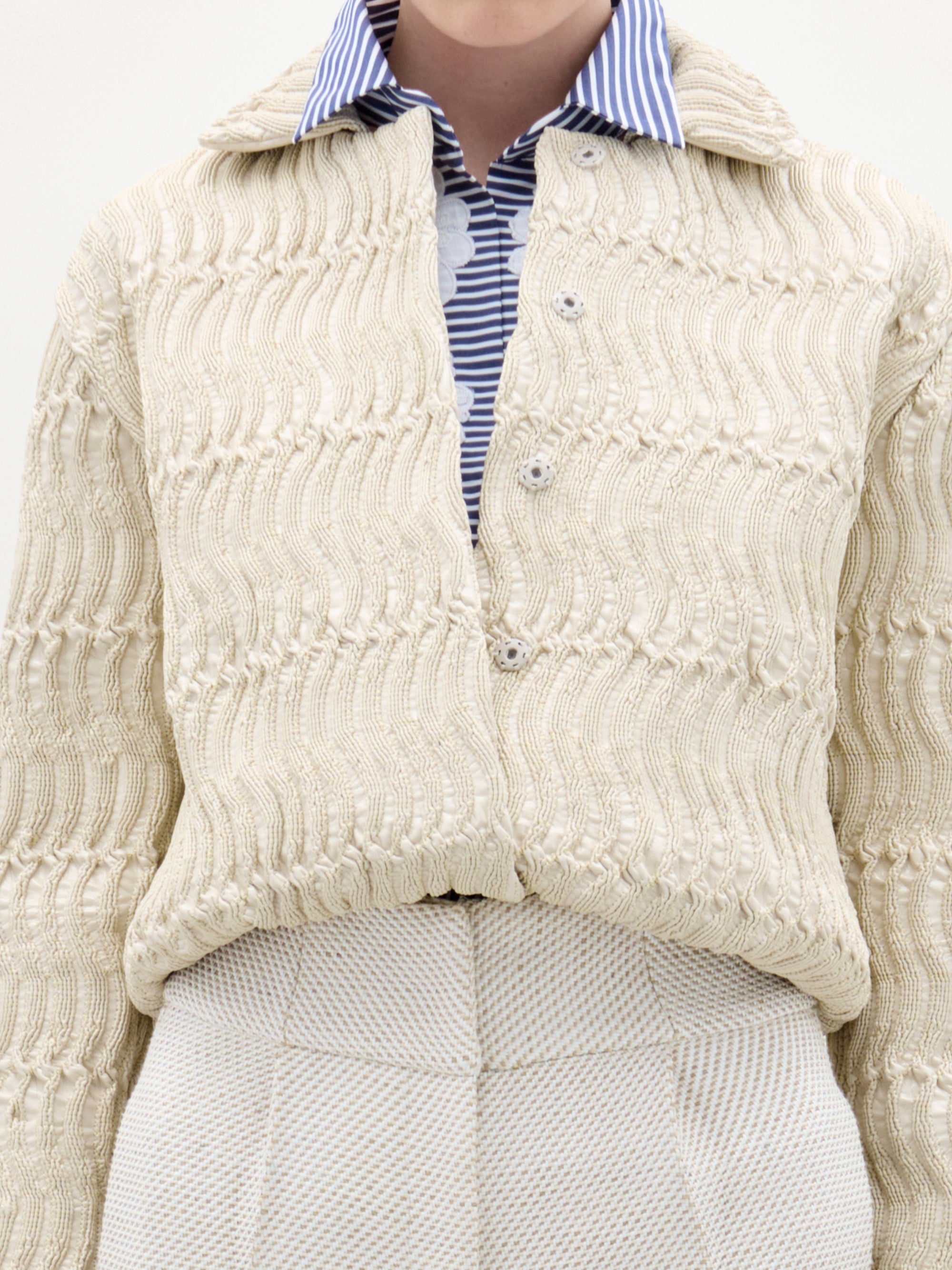 Close-up of a person wearing a cream knitted cardigan over a striped shirt.