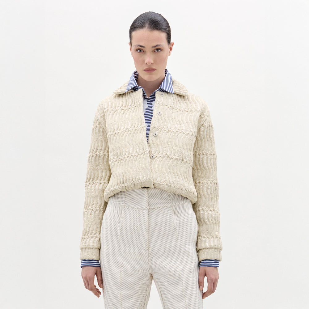 Woman wearing a cream knitted cardigan over a striped shirt on a white background