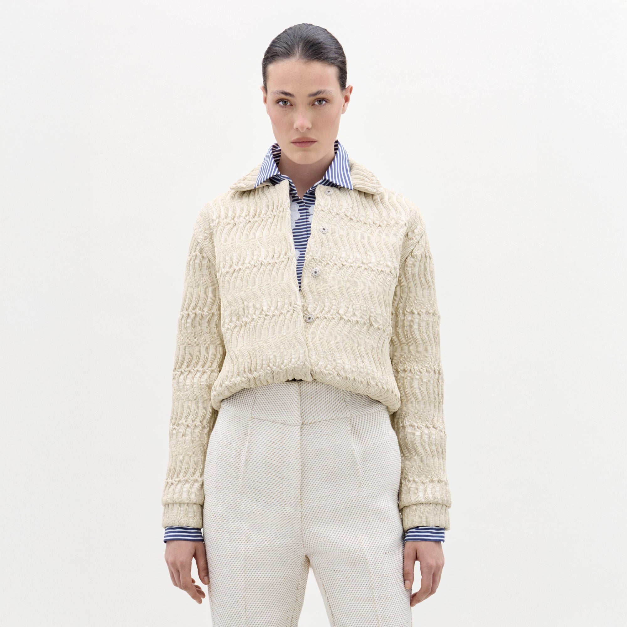 Woman wearing a cream knitted cardigan over a striped shirt on a white background