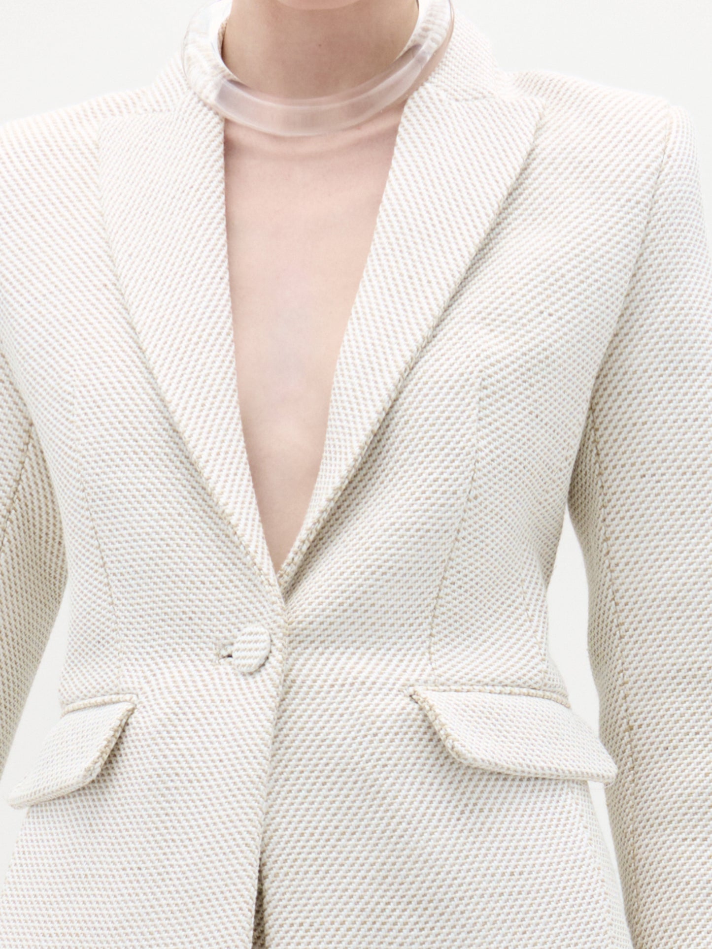 Close-up of a textured white blazer with a clear plastic neckpiece.