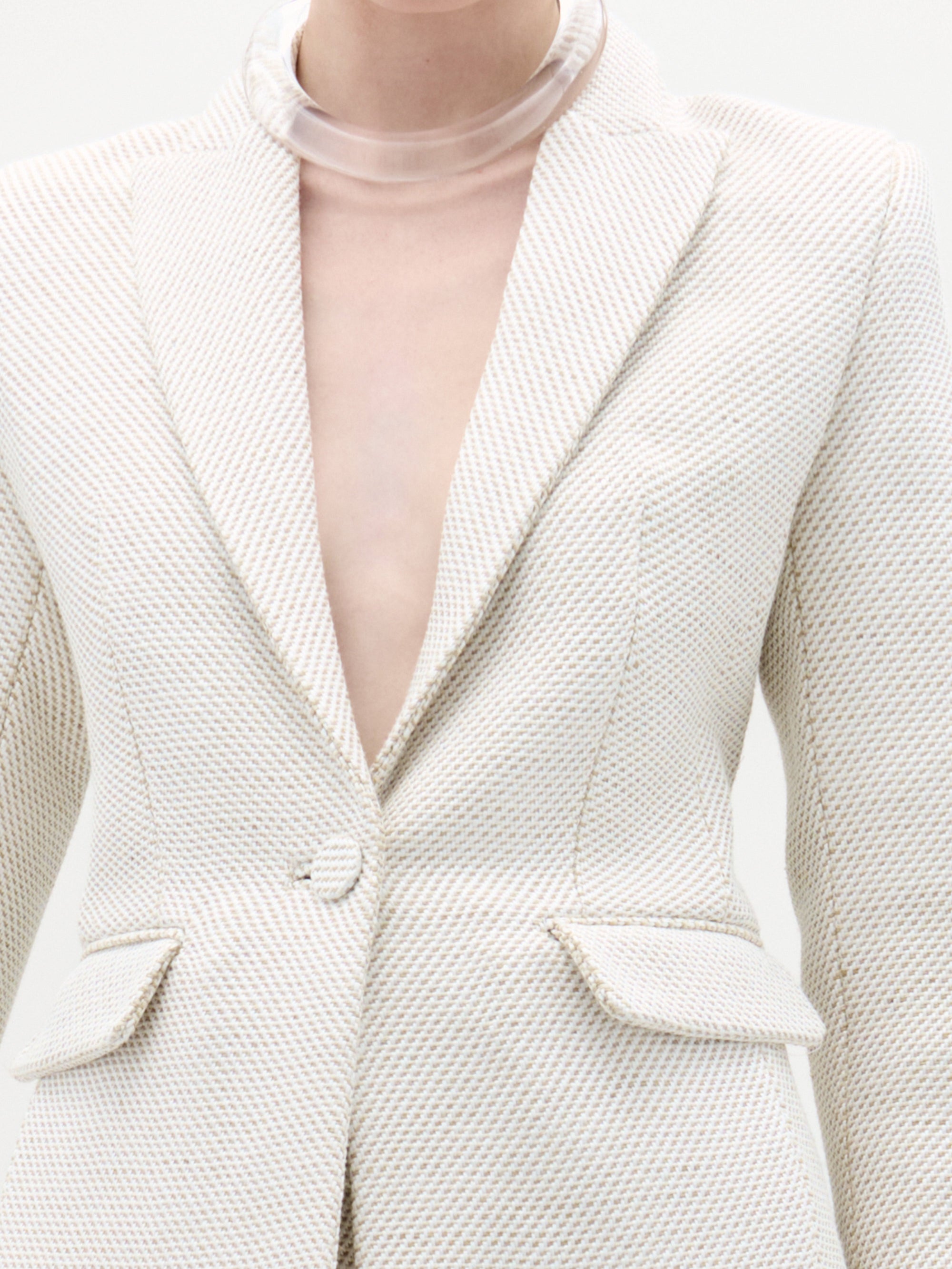 Close-up of a textured white blazer with a clear plastic neckpiece.