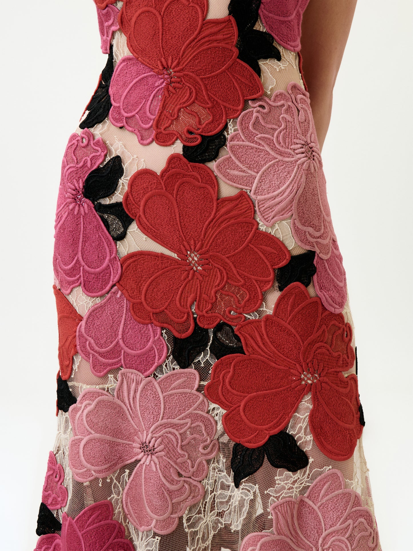 A close-up of the Vanessa Dress shows large red, pink, and black floral appliqués on sheer Italian lace, with part of a person’s arm visible on the right.