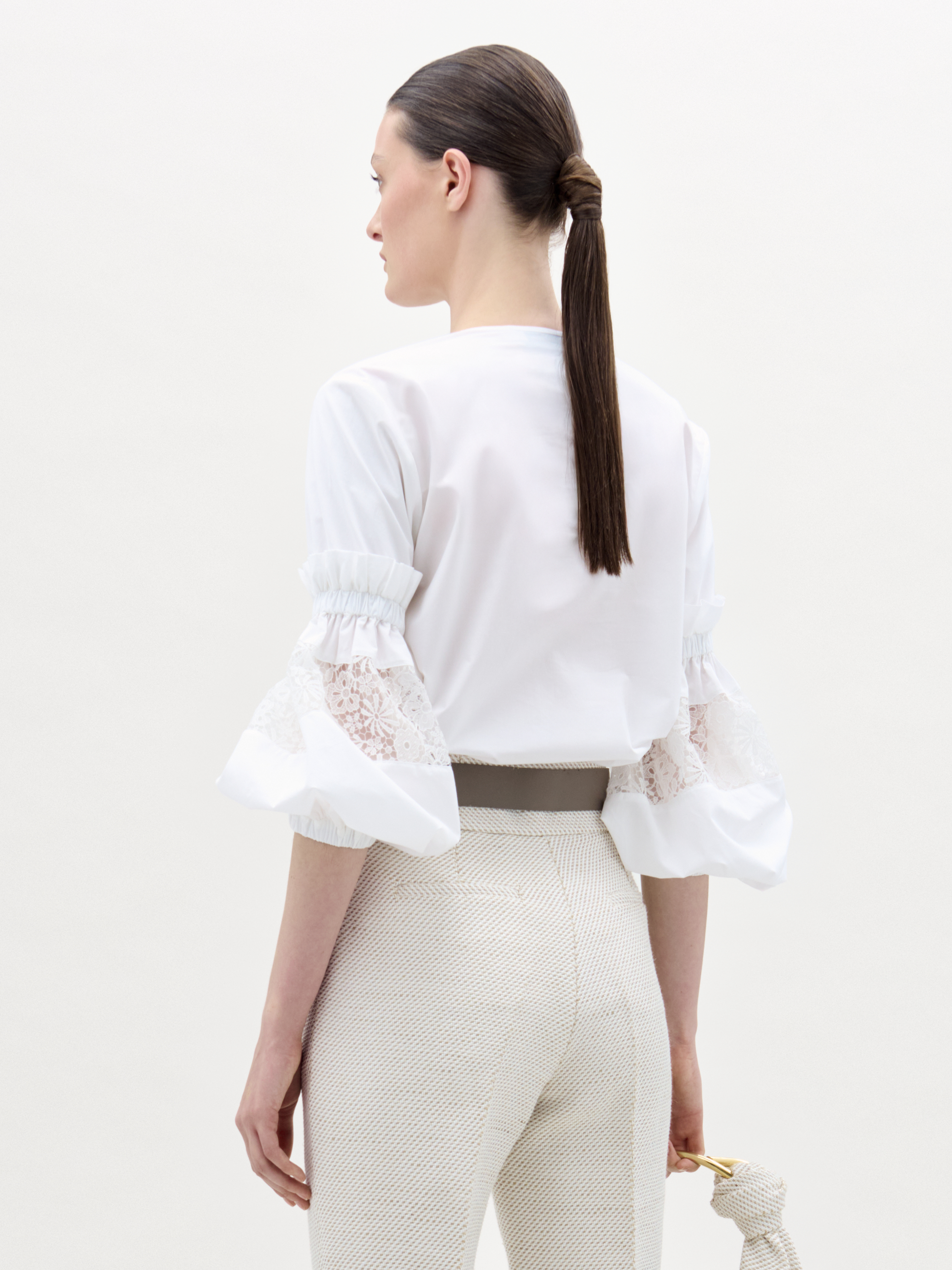 Woman wearing a white blouse with lace sleeves and beige pants on a white background