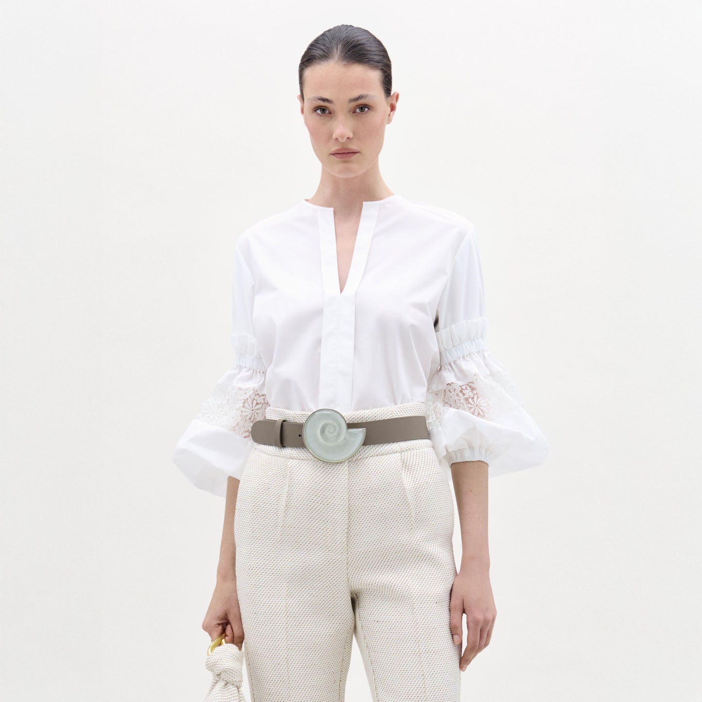 Woman wearing a white blouse and beige pants with a belt on a white background