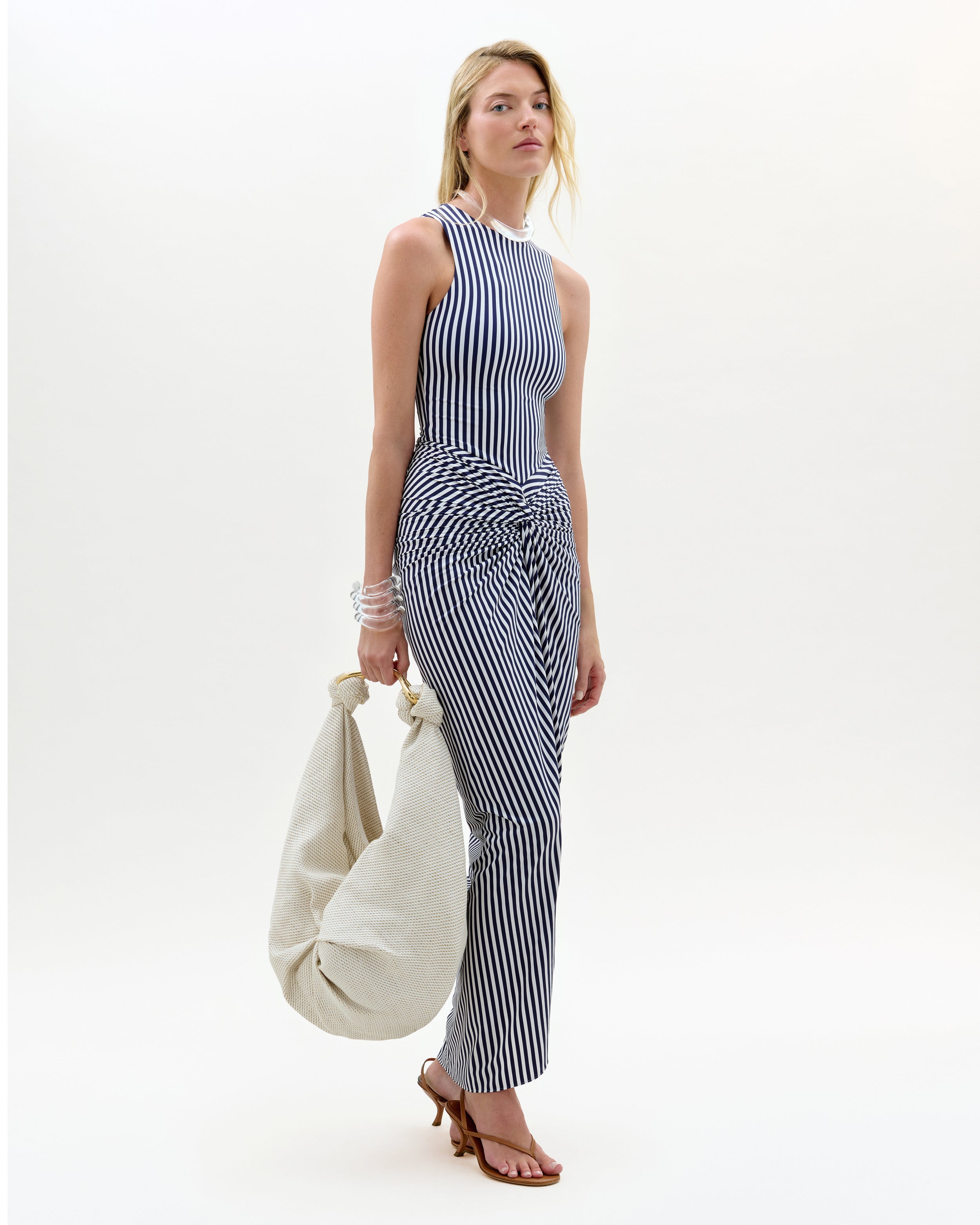 Woman wearing a black and white striped jumpsuit holding a beige bag on a white background
