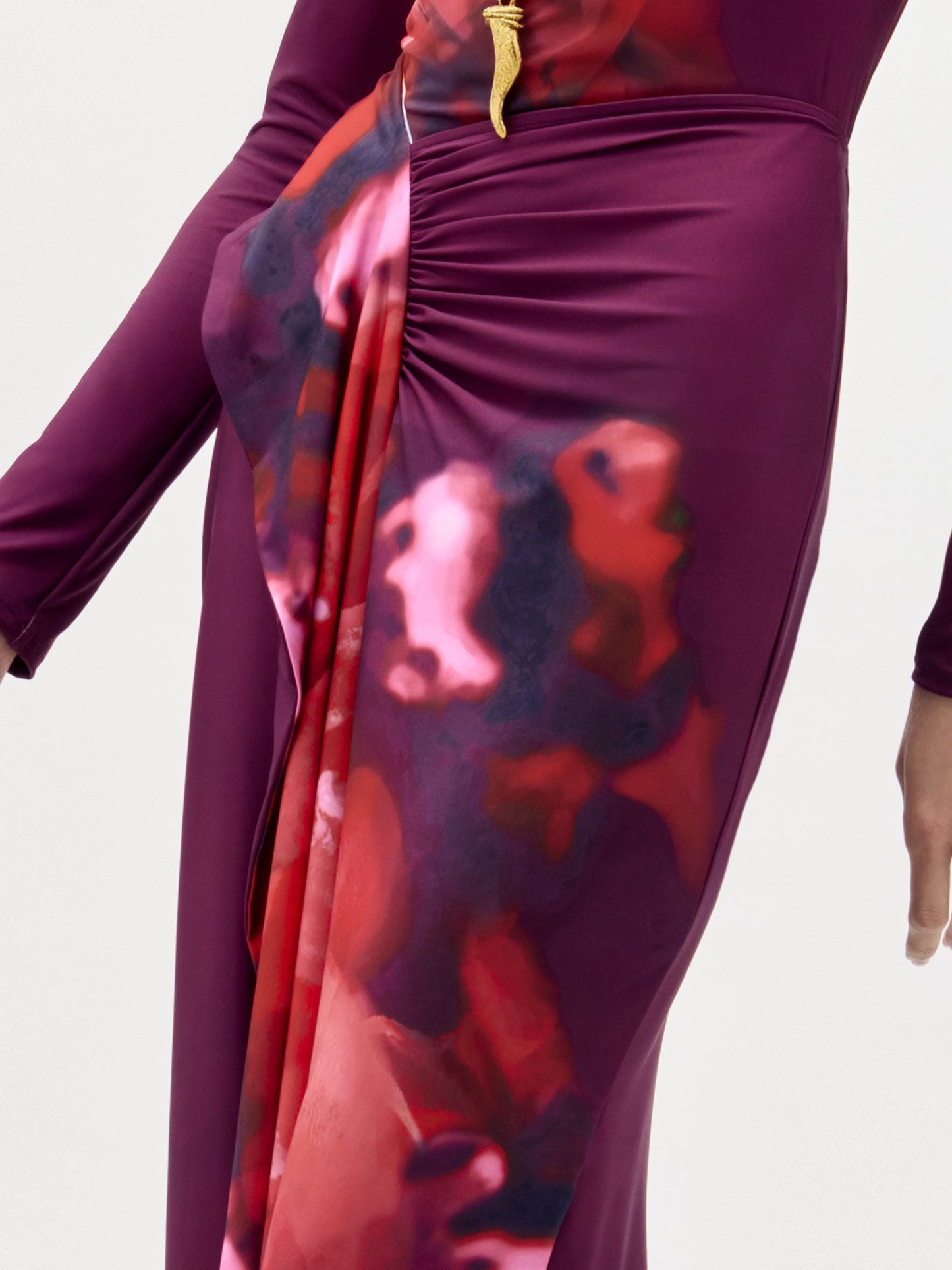 A woman models the Meissa Skirt, featuring a floor-length magenta design with a red and purple abstract pattern, paired with layered necklaces, against a plain white background.