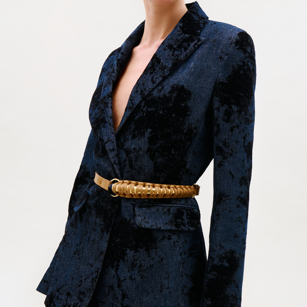 A person wearing a dark blue velvet blazer with a deep neckline, styled with the distinctive Ife Belt, stands against a plain light background.