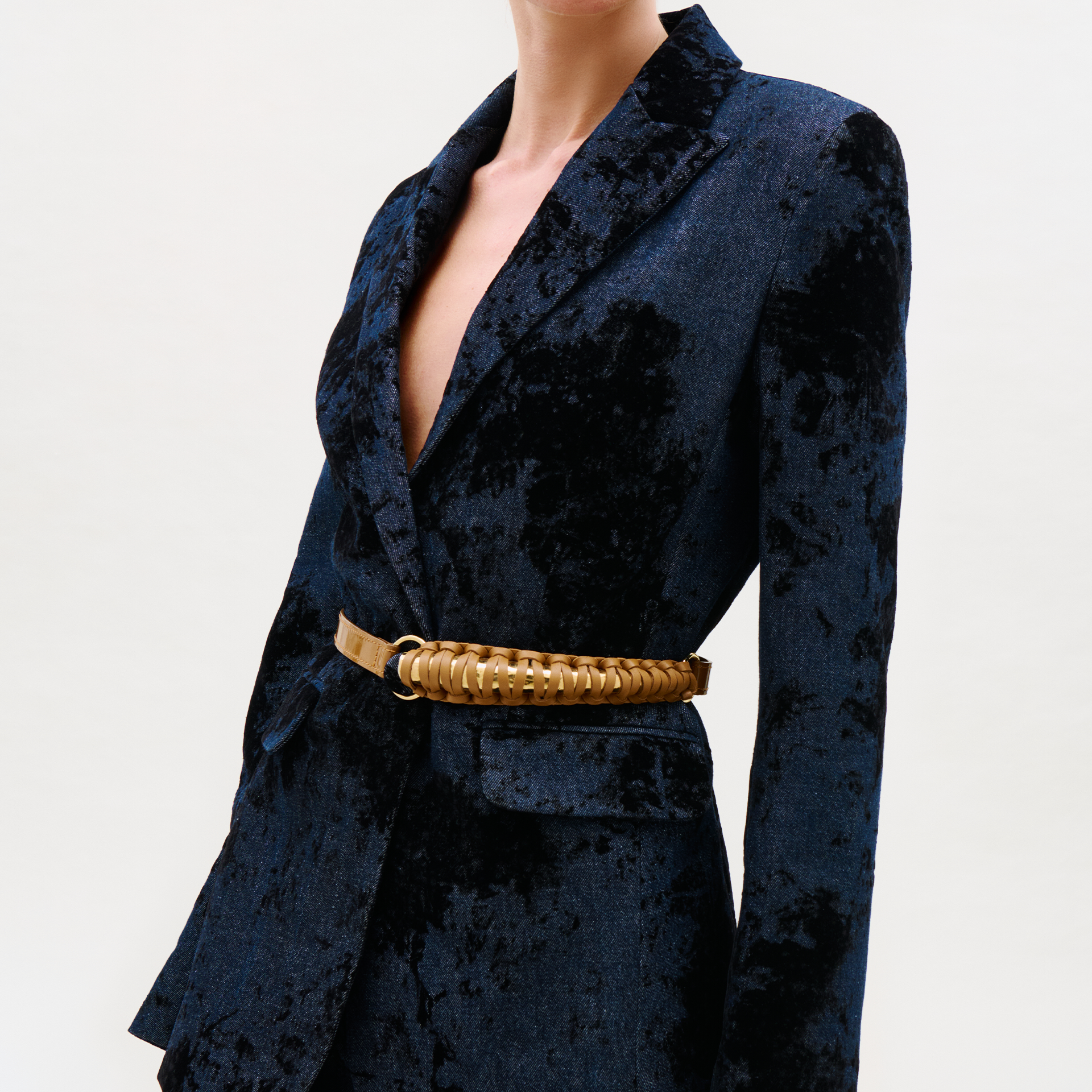 A person wearing a dark blue velvet blazer with a deep neckline, styled with the distinctive Ife Belt, stands against a plain light background.