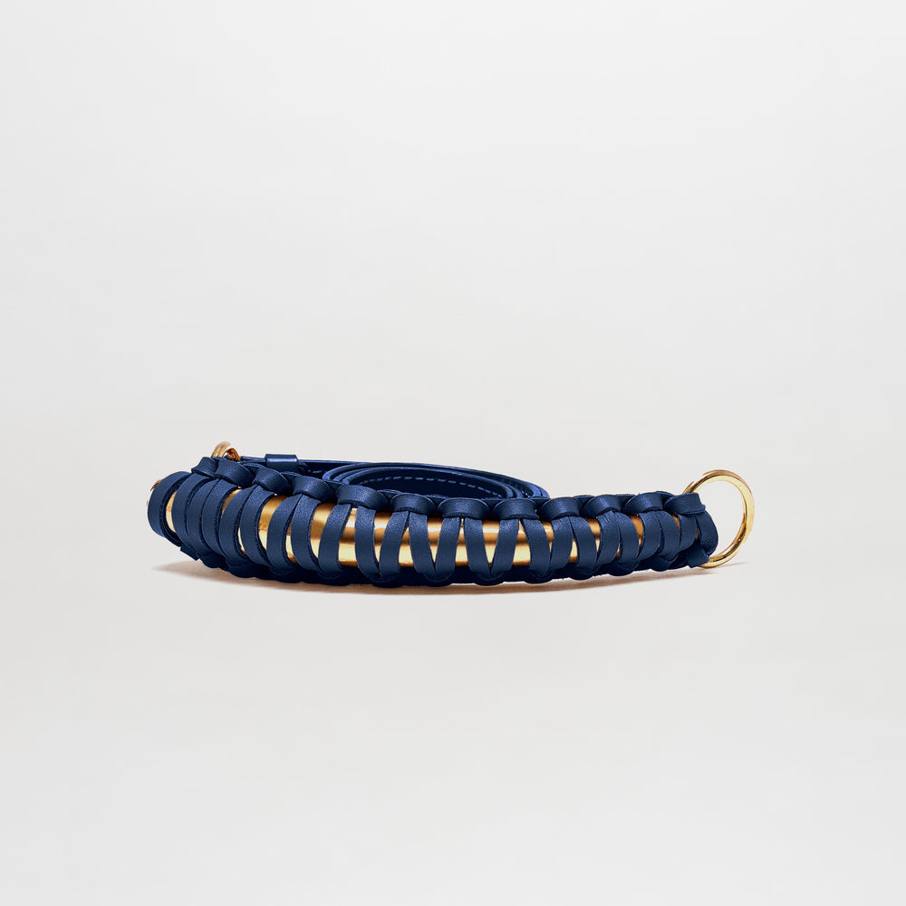 The Ife Belt is a coiled navy blue leather belt featuring gold metal rings at both ends, crafted in Colombia and displayed against a plain light background.