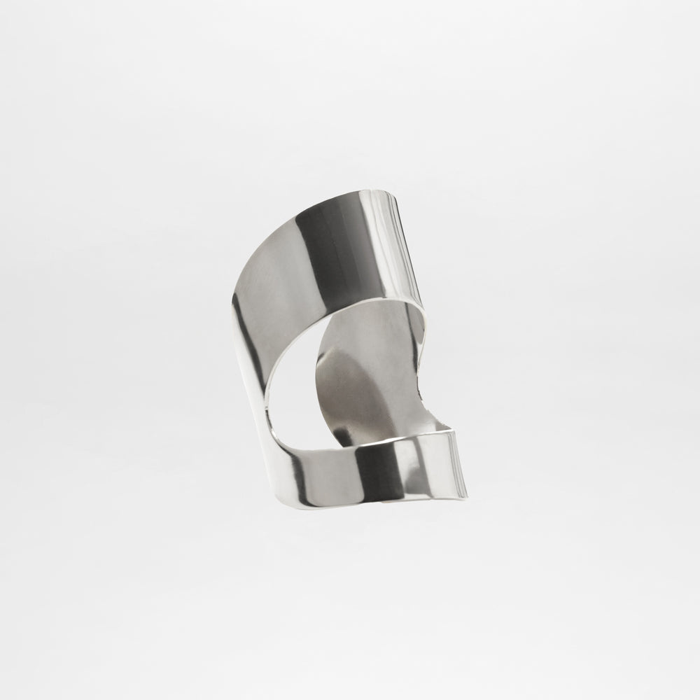 The Artemis Cuff is a smooth, abstract silver metal sculpture with curved and folded surfaces, resembling a silver plated bracelet, showcased against a plain white background.