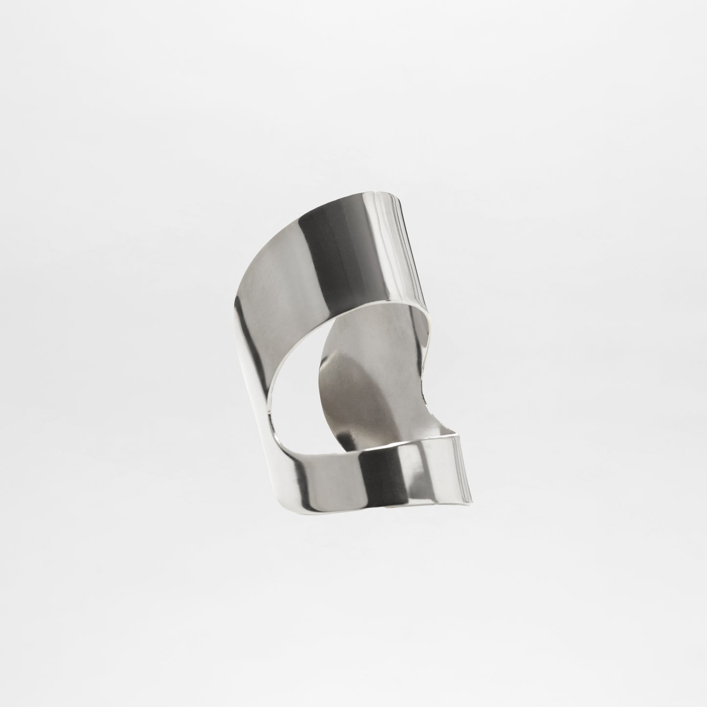 The Artemis Cuff is a smooth, abstract silver metal sculpture with curved and folded surfaces, resembling a silver plated bracelet, showcased against a plain white background.