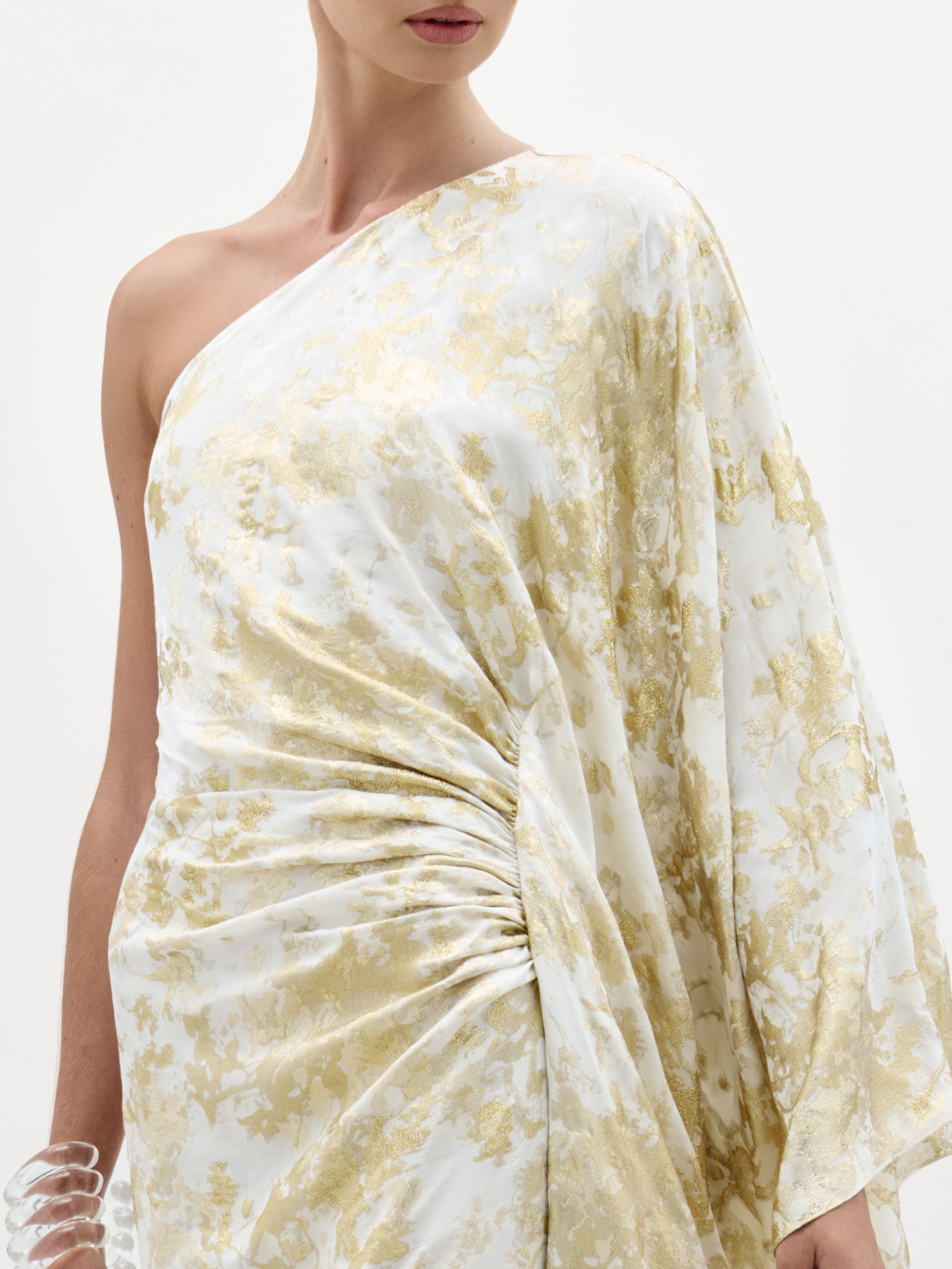 Woman wearing a white and gold floral one-shoulder dress on a plain background