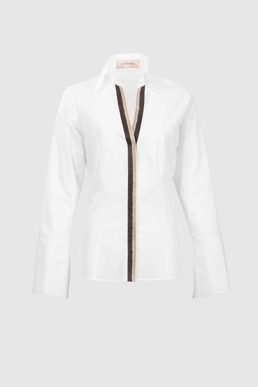 The Andrea Blouse is a white, long-sleeve, collared shirt made from 100% Portuguese cotton, featuring a black and beige vertical front stripe. Shown on a light grey background.
