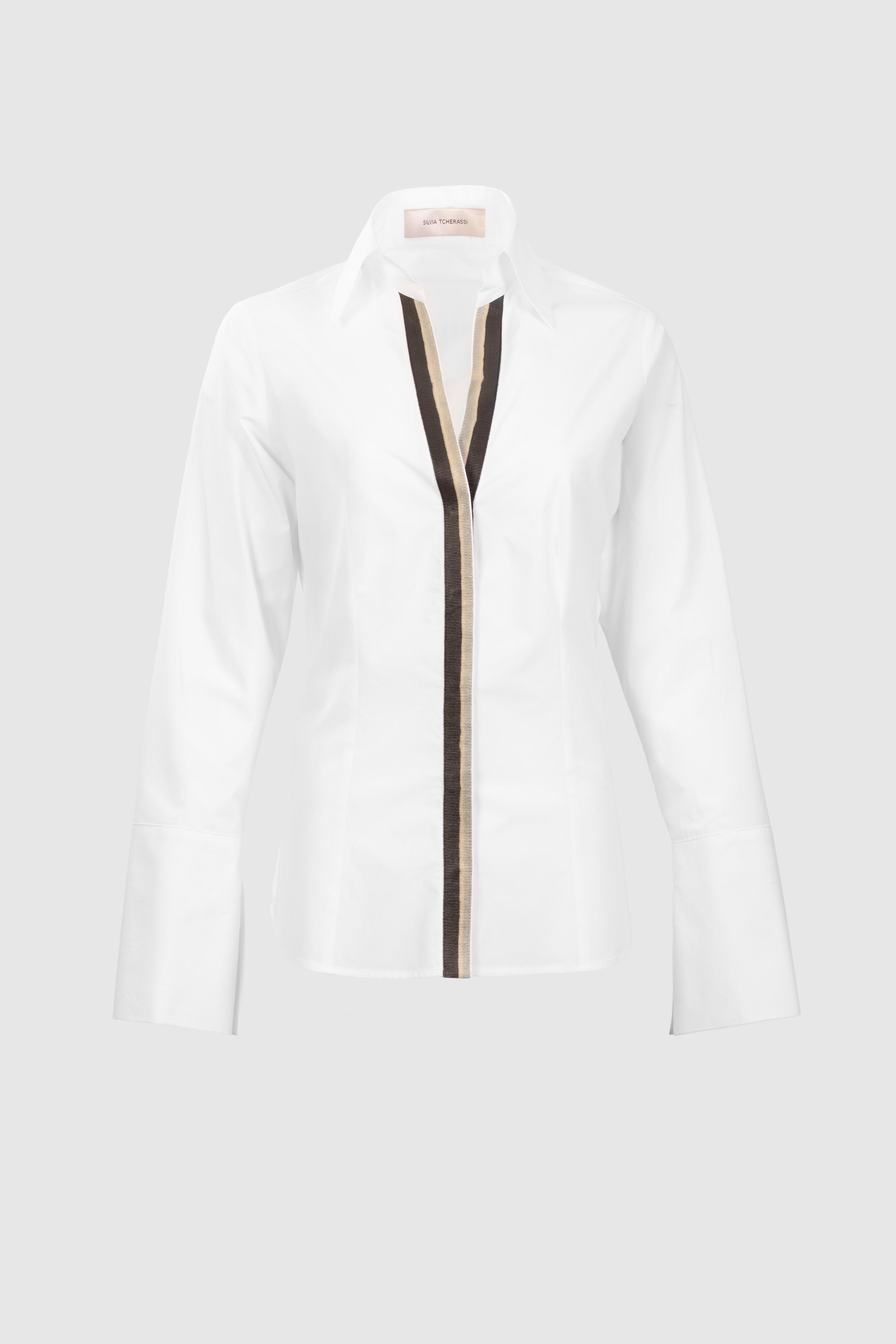 The Andrea Blouse is a white, long-sleeve, collared shirt made from 100% Portuguese cotton, featuring a black and beige vertical front stripe. Shown on a light grey background.