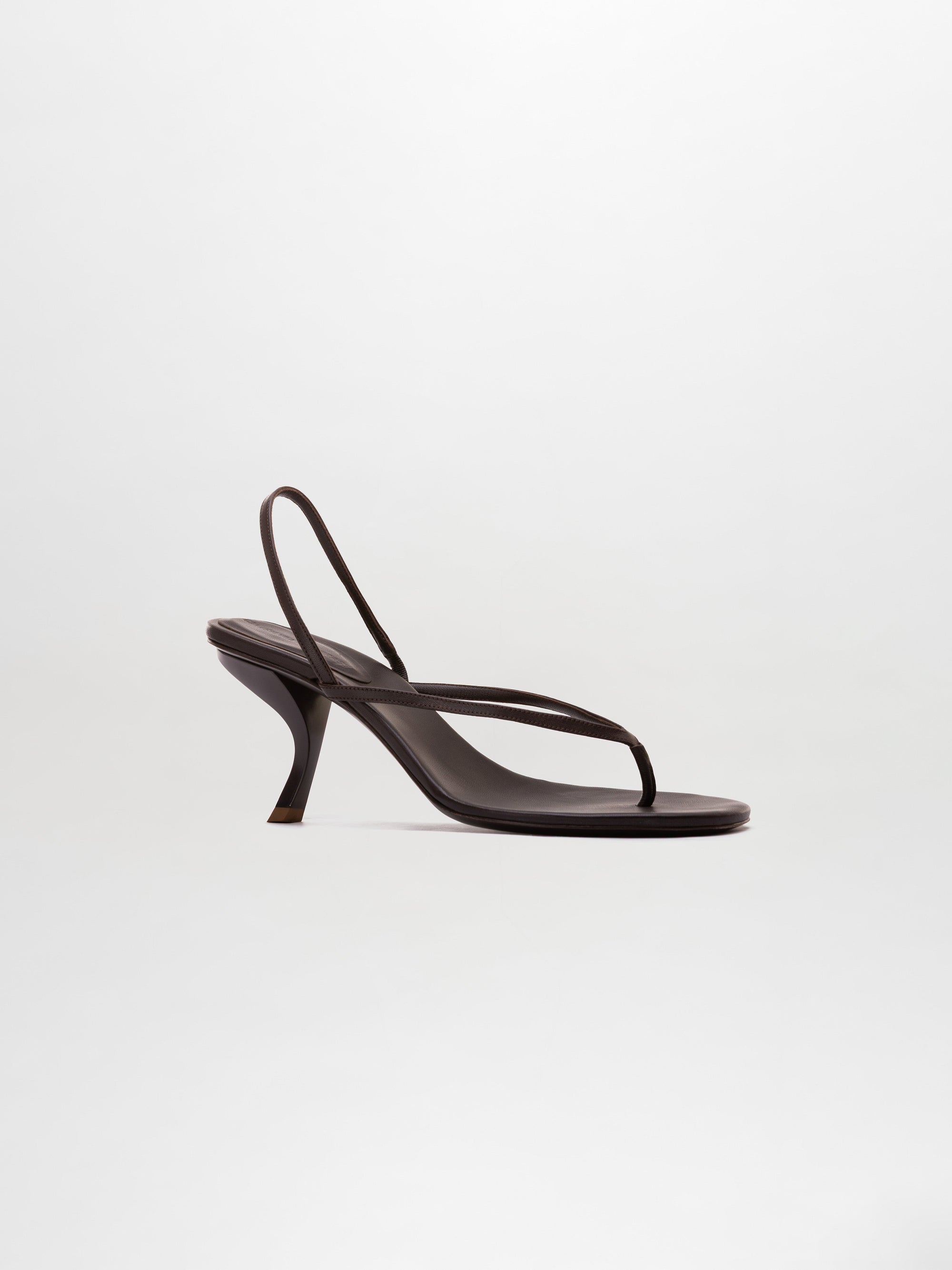 The Aurora Heels are black strappy sandals featuring a thin thong-style toe strap and a curved heel, showcased against a plain light background.