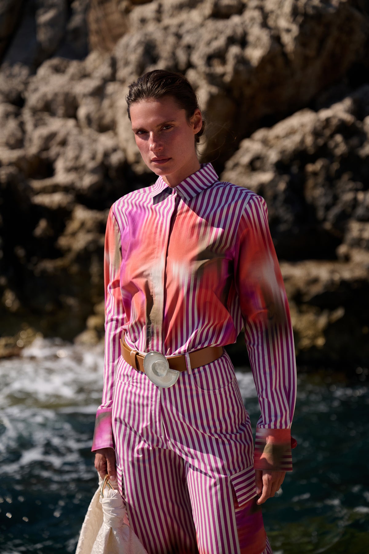 Person wearing a pink and white striped outfit with a belt, standing against a rocky background.