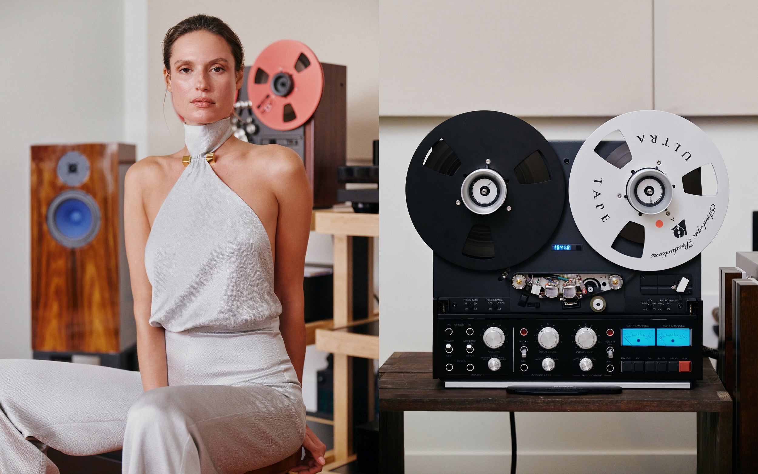 A woman in a white halter-neck dress sits beside a large vintage reel-to-end cassette recorder on a wooden table, with speakers and wooden shelving in the background.