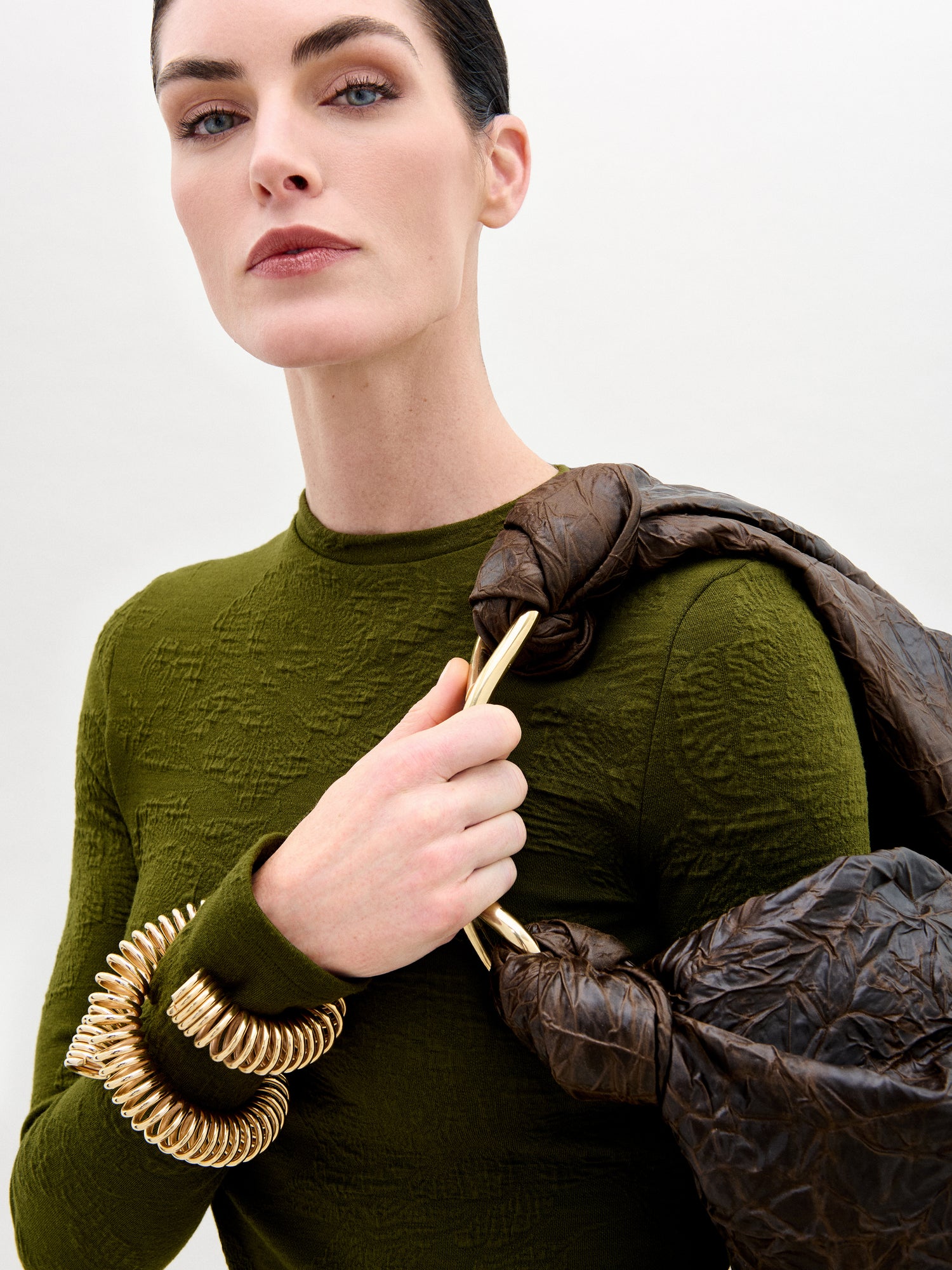 Model wearing green shirt while holding a maroon purse.