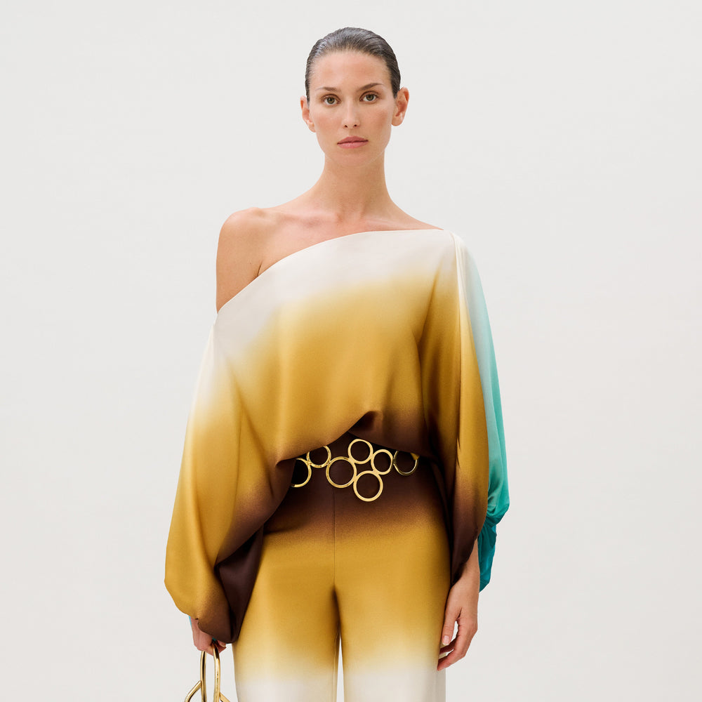 Model wearing the Bellagio Blouse, an off-the-shoulder, ombre-toned Italian silk top with one long, loose sleeve and a gold-tone circular link belt at the waist.